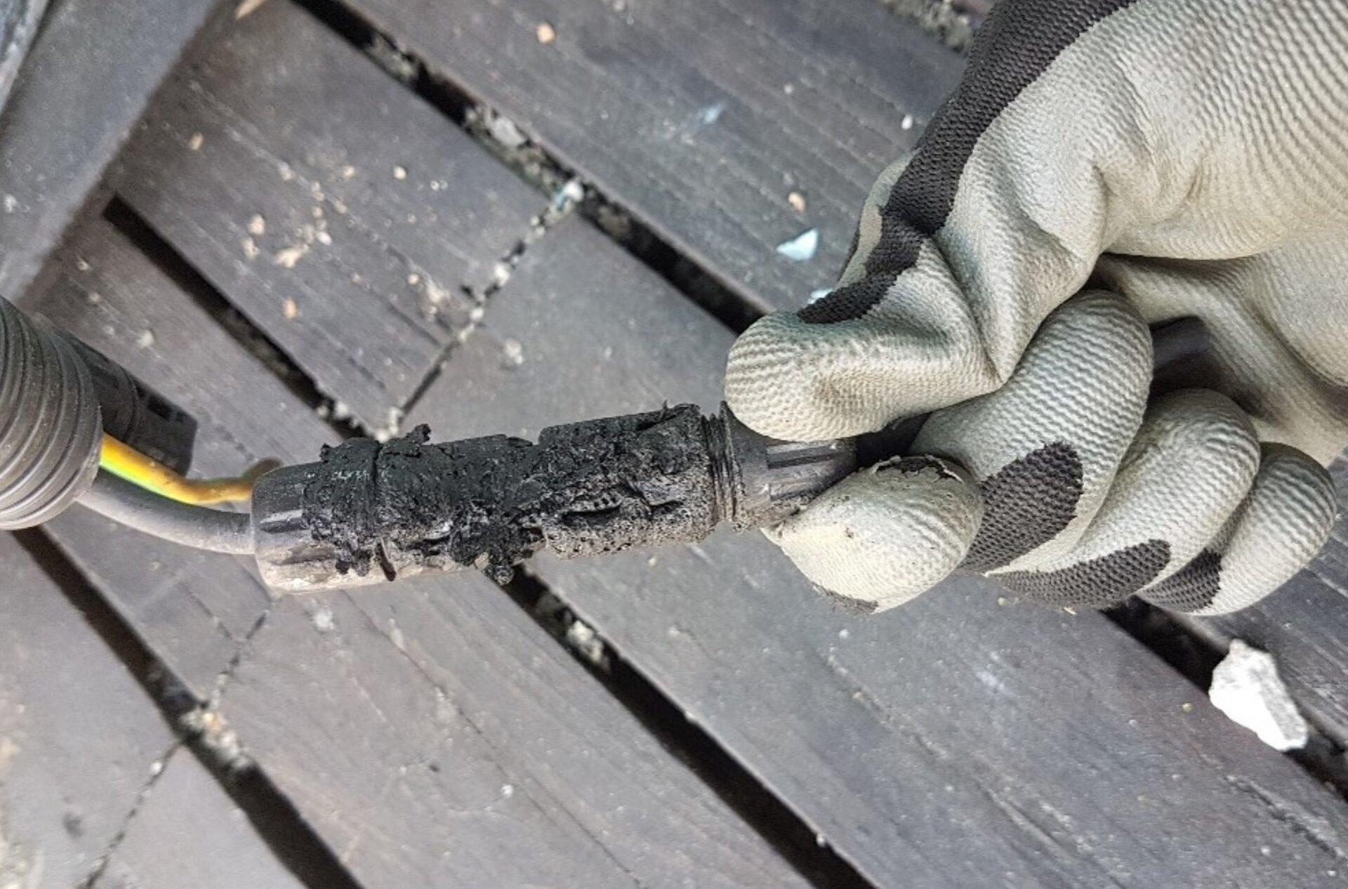 Zdjęcie przedstawia skutki zastosowania niekompatybilnych złączek MC4 i H4. Monter dłonią w rękawiczce trzyma spaloną złączkę. 
