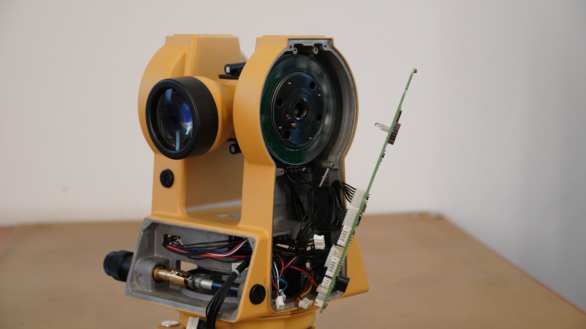Na zdjęciu przedstawiono boczne ujęcie teodolitu. Po lewej stronie widoczny jest obiektyw lunety, a na prawo od niego boczny panel ze zdemontowaną płytką modułu sterującego. W tym miejscu widoczna jest sieć cienkich przewodów zakończonych stykami. Pod obiektywem znajduje się miejsce, w którym był zamontowany wyświetlacz.