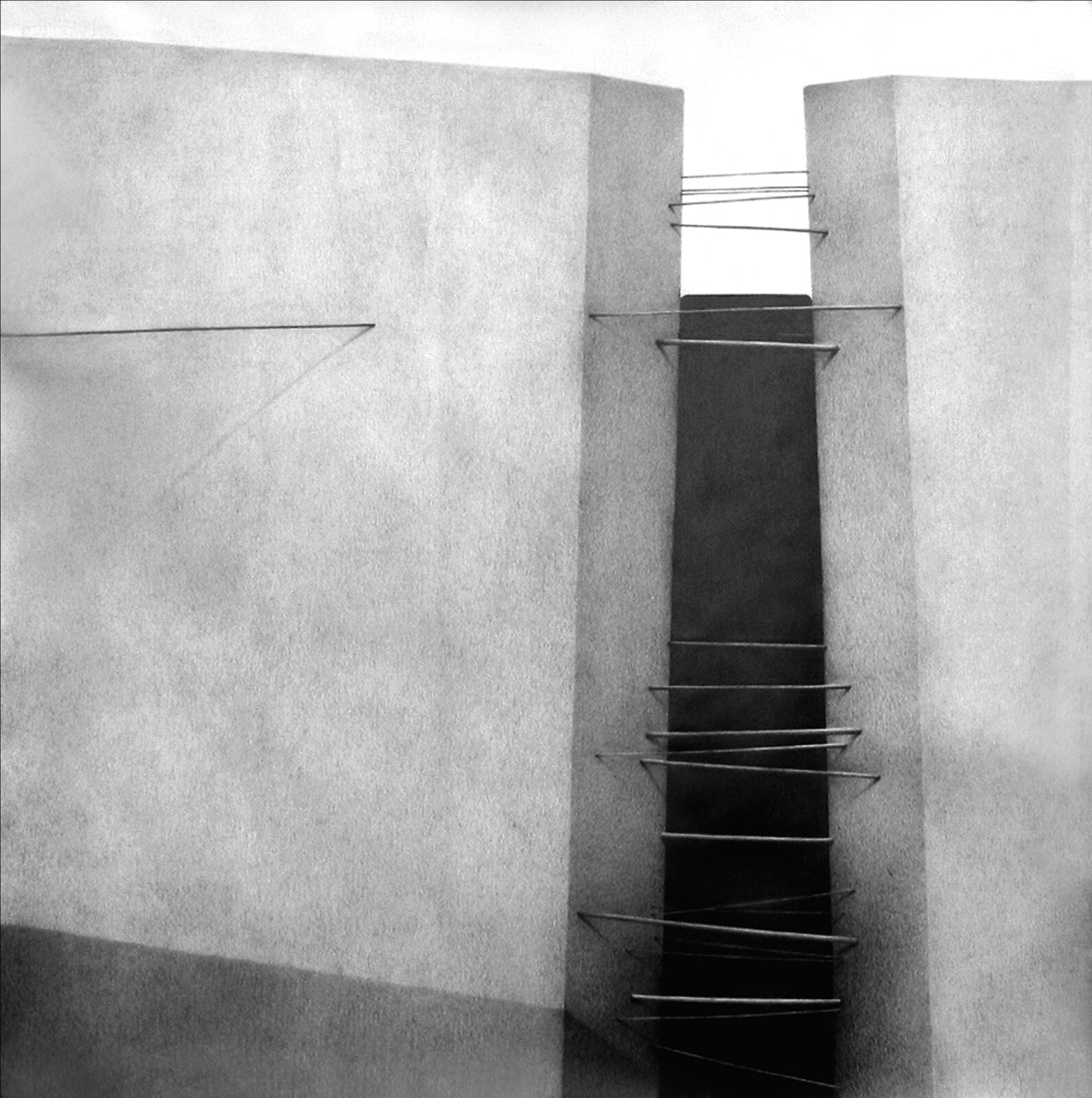 Ilustracja przedstawia rysunek „Wejście II”, autorstwa Weroniki Tadaj‑Królikiewicz. Kwadratowa kompozycja ukazuje dwa betonowe bloki, pomiędzy którymi po prawej stronie rysunku znajduje się wąskie przejście, poprzecinane cienkimi prętami łączącymi ściany. Jeden z kabli przebija bryłę bloku po lewej stronie. Wychodząc z niej, ciągnie się aż poza kadr obrazu. Tło rysunku stanowi płaska płaszczyzna podzielona na górną, białą część oraz dolną, szerszą, czarną część, która widoczna jest jedynie jako wąski, ciemny pas pomiędzy ścianami przejścia. Praca wykonana została przy pomocy ołówka na białym papierze.