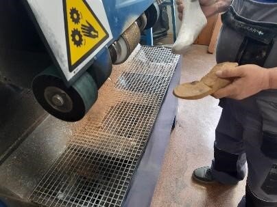 Zdjęcie przedstawia maszynę do szlifowania i osobę trzymającą w rękach odlew gipsowy oraz wkładkę z płyty suberytowej.