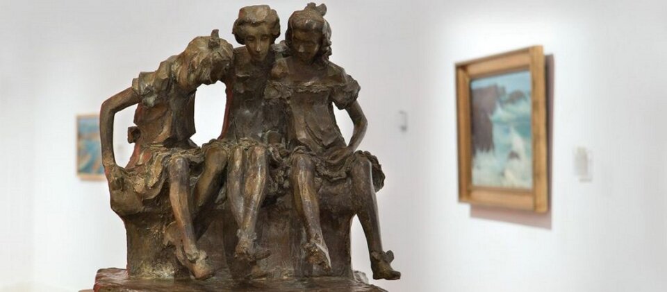 Ilustracja przedstawia rzeźbę pt. „Ławka” autorstwa Ludwika Pugeta. Rzeźba ukazuje trzy siedzące, machające nogami i zajęte żywą rozmową pensjonarki.