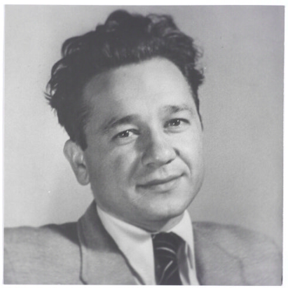 Zdjęcie przedstawia dojrzałego mężczyznę. Jego twarz jest okrągła, czoło wysokie. Mężczyzna ma szeroki nos. Jego włosy są ciemne, falujące, zaczesane ku górze. Ubrany jest w koszulę, garnitur  krawat.