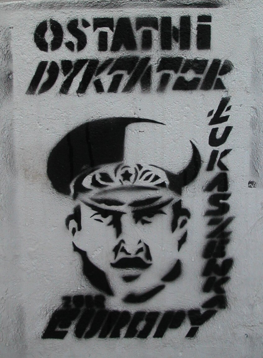 Zdjęcie przedstawia grafikę namalowaną na ścianie. W centralnej części znajduje się twarz mężczyzny w wojskowej czapce. Widoczny jest napis: ostatni dyktator Europy, Łukaszenka.