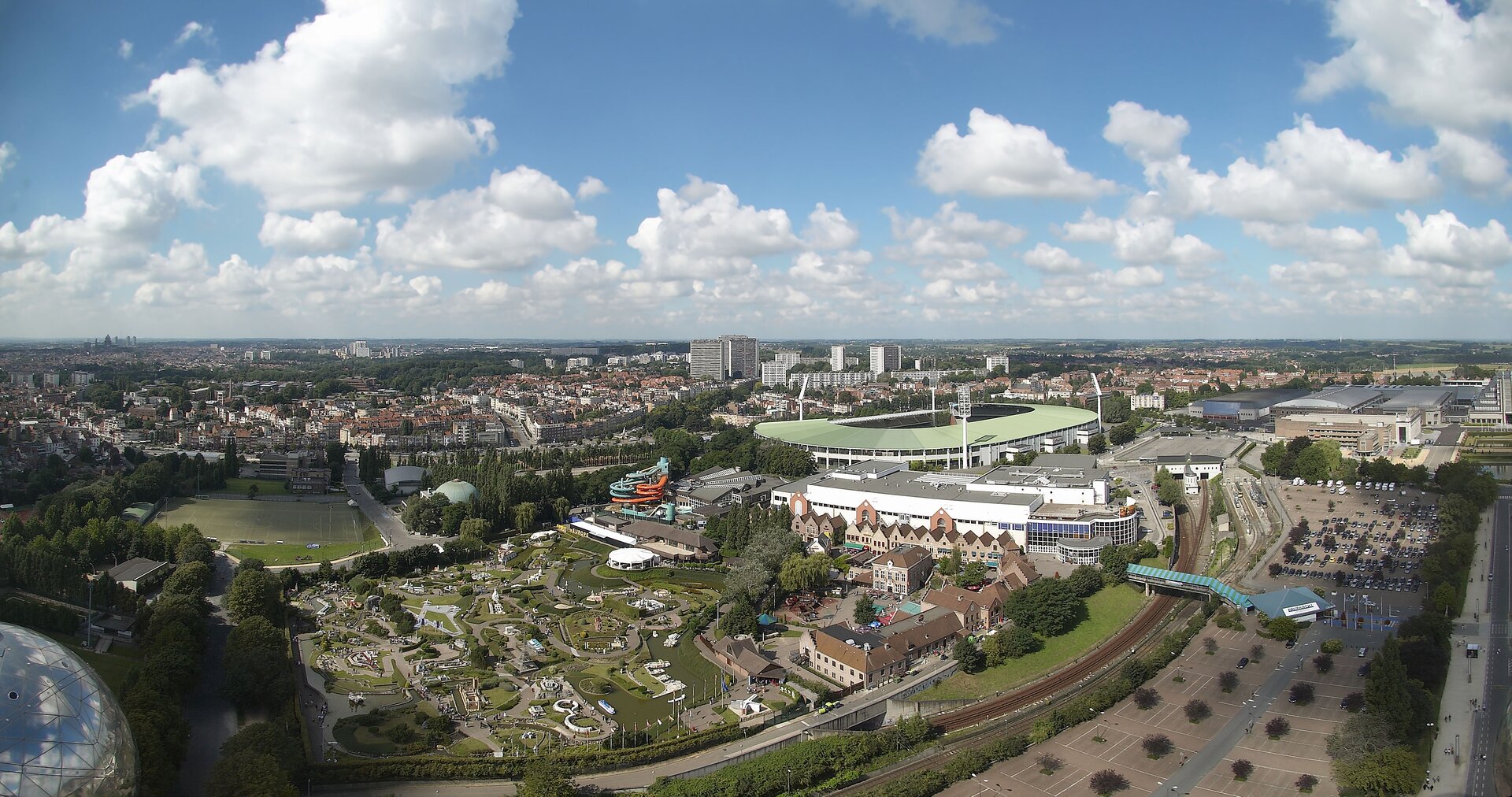 Na zdjęciu panorama Brukseli z widocznym na pierwszym planie parkiem miniatur Mini-Europa. Dalej kompleks obiektów sportowych ze stadionem i zjeżdżalnią. Z prawej strony linia kolejowa i rozległe parkingi.