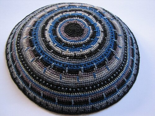 Ilustracja przedstawia niewielkie, okrągłe nakrycie głowy, wykonane na drutach bądź szydełku, różnokolorowe. Jest to jarmułka noszona przez Żydów. Mężczyźni noszą ją na czubku głowy. 