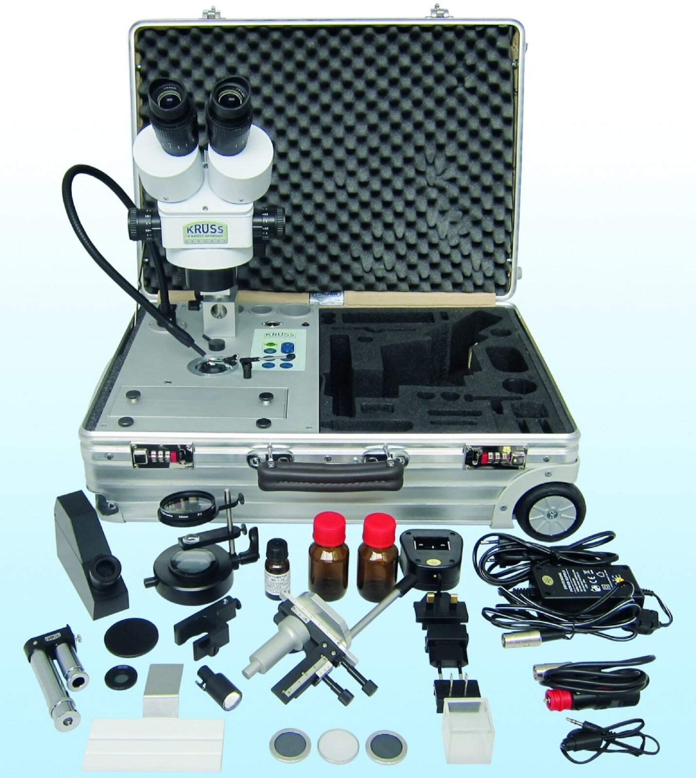 Ilustracja przedstawia podręczny zestaw narzędzi gemmologa. Na obrazku obecne są między innymi mikroskop, małe buteleczki z nieznanymi substancjami, kable oraz lupa.