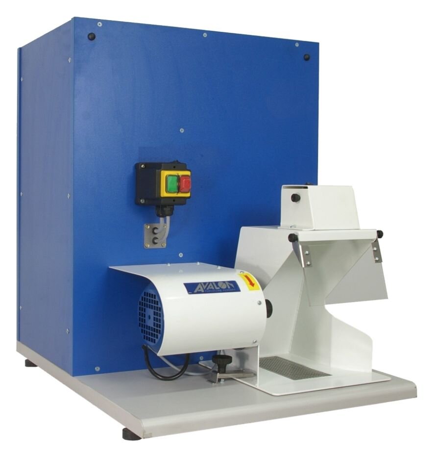 Zdjęcie przedstawia polerkę stołową. To maszyna z niewielkim blatem, na którym zamontowany jest pod osłoną silnik. Po jego prawej stronie znajduje się osłona zabezpieczająca przed pyłem polerskim i opiłkami. Za silnikiem znajduje się sześcienna obudowa, na której zamontowane są włączniki w kolorze zielonym i czerwonym.