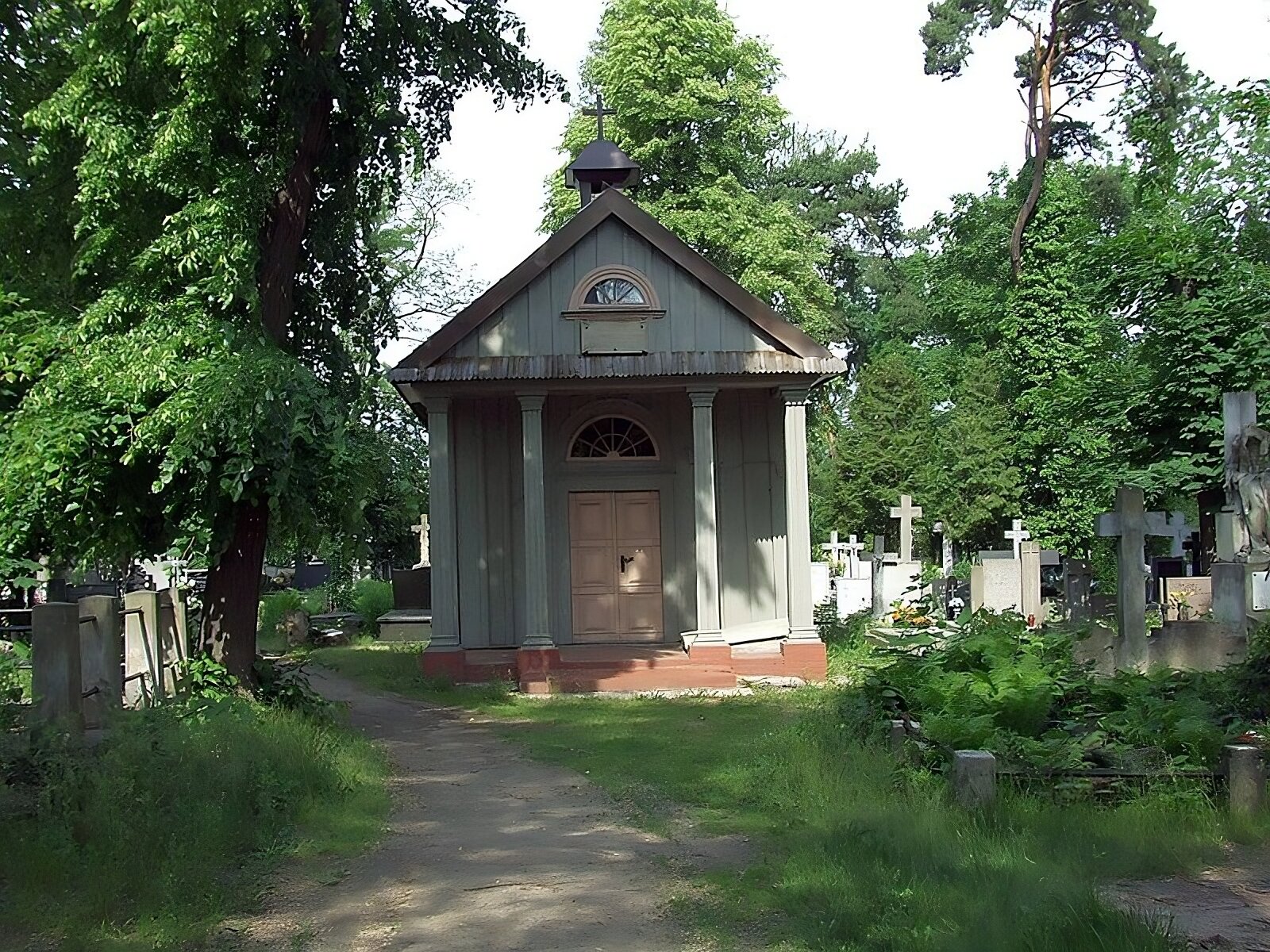Zdjęcie współczesne przedstawia widok na ścianę frontową kaplicy rodziny Marylskich na cmentarzu. Trójkątny tympanon wieńczy szczyt budynku, na którego dachu znajduje się wieżyczka z krzyżem. W centralnej części fasady widoczne cztery kolumny podpierające tympanon. Drzwi drewniane, dwuskrzydłowe z klamką. Nad nimi witraż w formie półokręgu. Dookoła kaplicy groby cmentarne z krzyżami, po lewej stronie obiektu widać ubitą ścieżkę i drzewo. Na dalszym planie cmentarza pojedyncze drzewa.