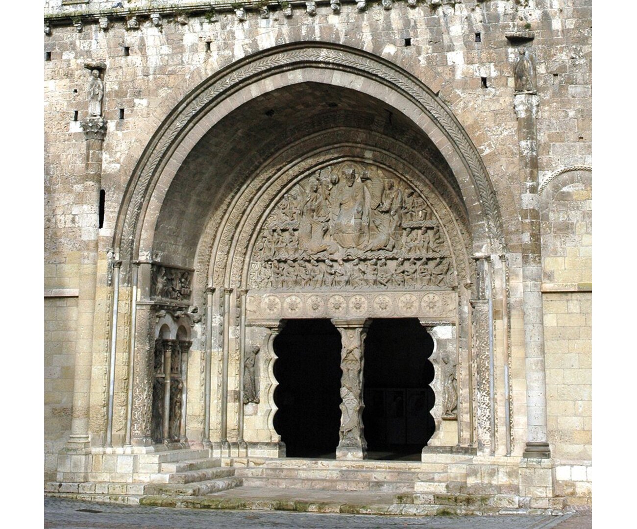 Fotografia barwna przedstawiająca tympanon kościoła w Moissac. Nad bramą uwidocznione elementy wyżłobień, sklepienia.