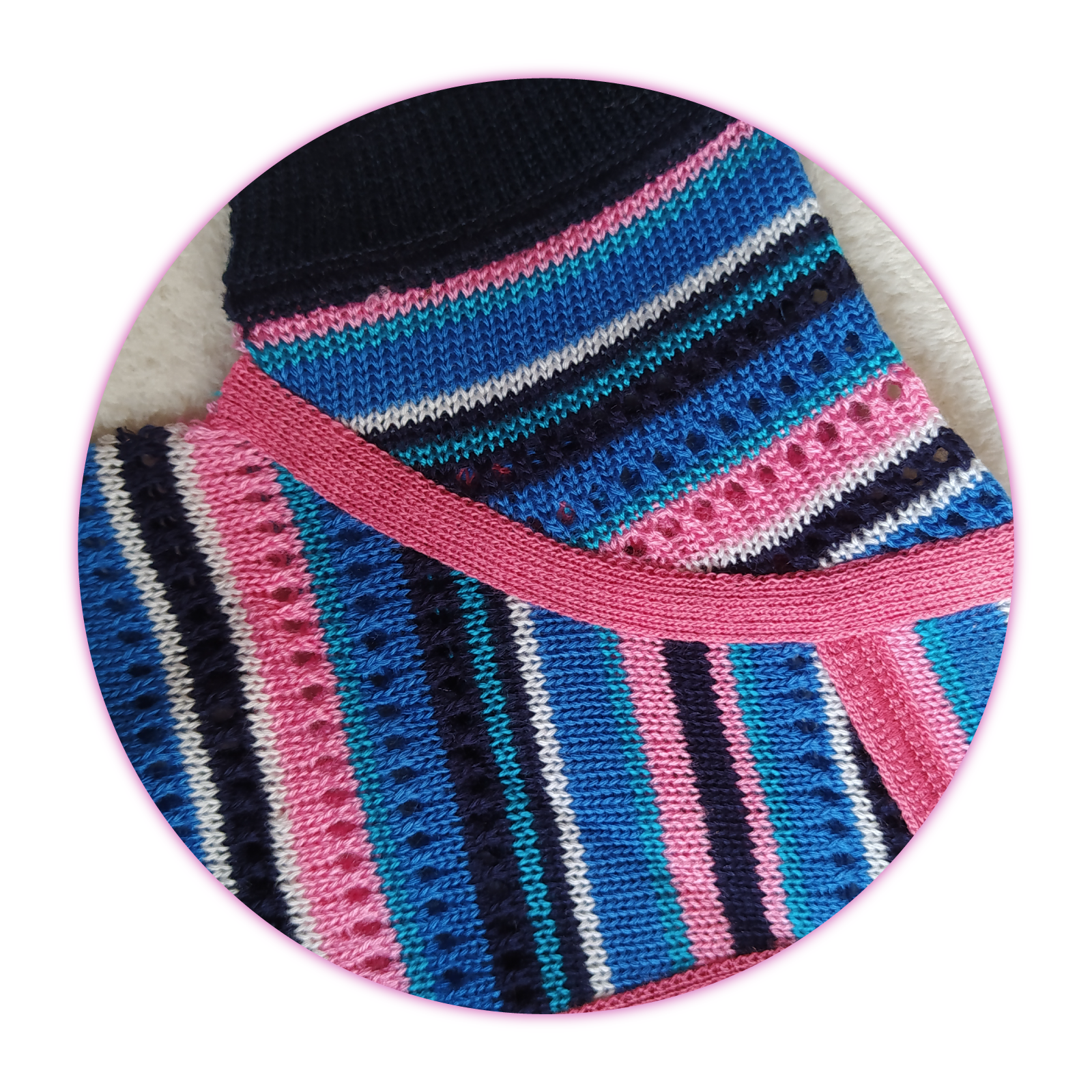 Zdjęcie przedstawia fragment dzianinowego wyrobu odzieżowego z krótkimi rękawami. Wyrób jest w kolorowe paski, ma różową lamówkę, wykończenie rękawów jest czarne.