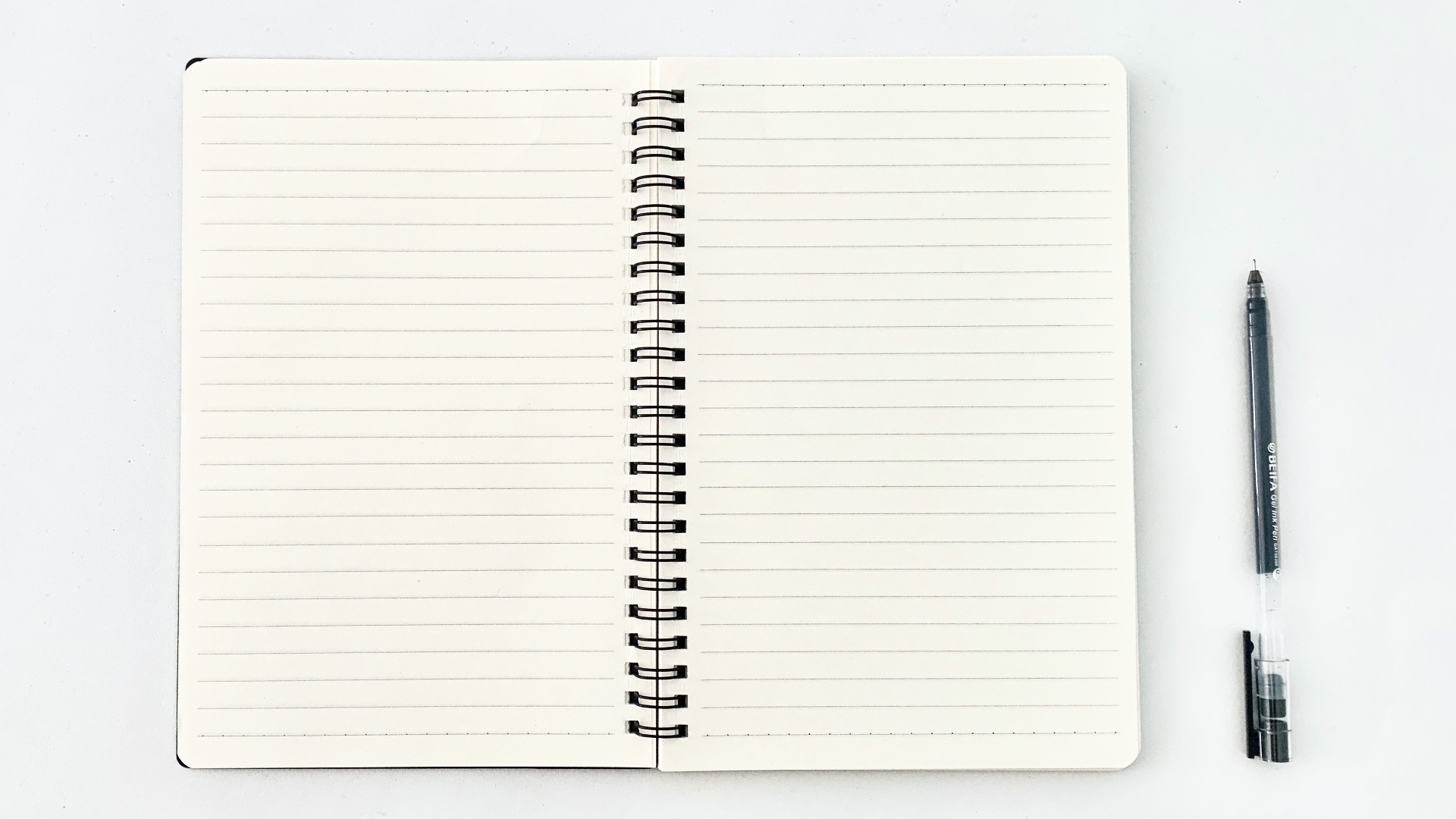 Na zdjęciu znajduje się kołonotatnik w linie. Obok notatnika leży długopis.