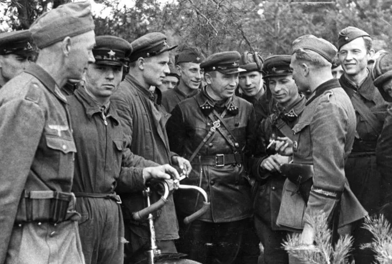 Kliknij, aby powiększyć Zdjęcie przedstawia żołnierzy w niemieckich i radzieckich mundurach. Stoją na przeciwko siebie. Uśmiechają się do siebie. Rozmawiają.