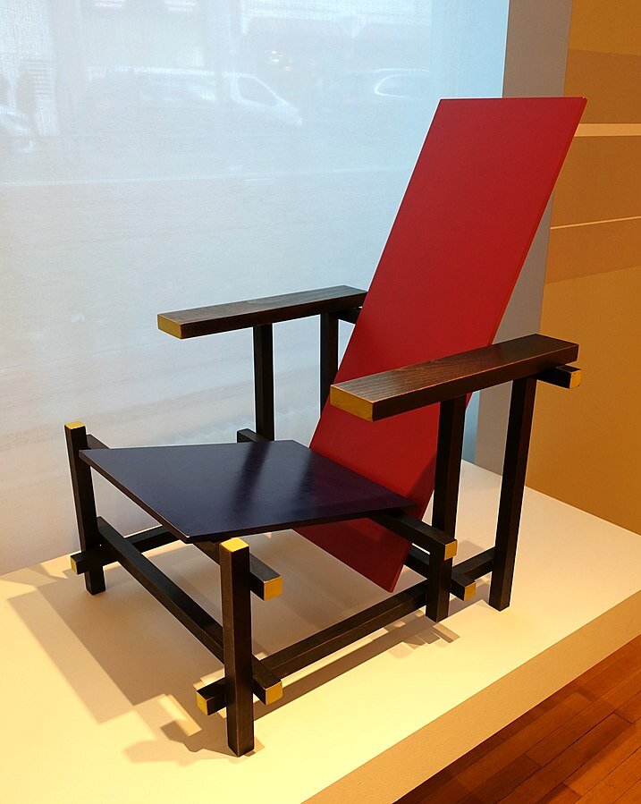 Ilustracja przedstawia krzesło zaprojektowane przez  Gerrita Rietvelda  [czytaj: gerita rtwelta]. Mebel jest kanciasty, posiada ostre krawędzie. Siedzisko fotela jest w zimnym kolorze (niebieskim), oparcie natomiast w kolorze gorącym (czerwonym). Zarówno siedzisko jak i oparcie nie są ustawione względem siebie pod kątem prostym, są przechylone tworząc kąt rozwarty. 