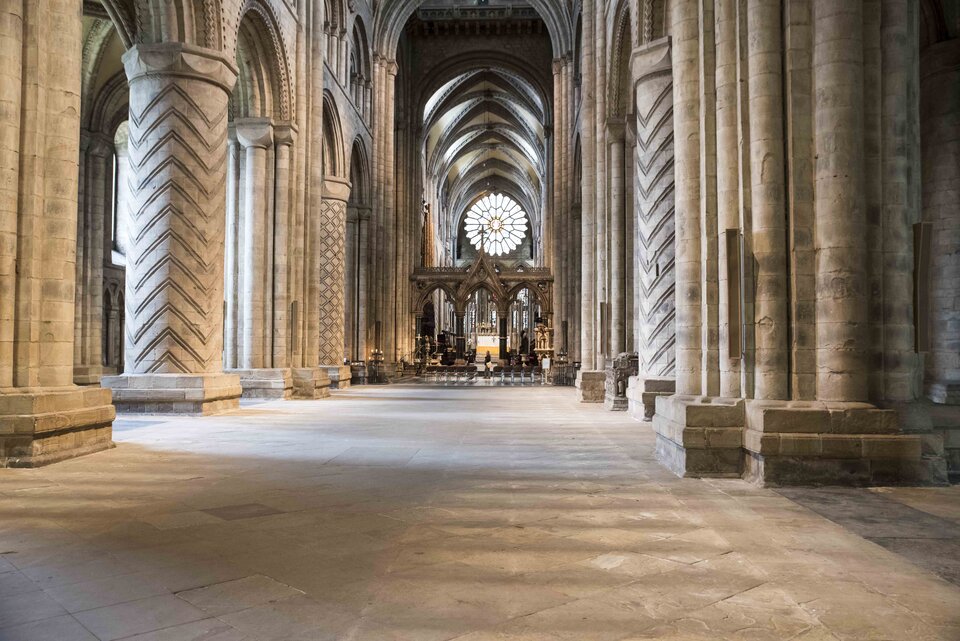 Ilustracja o kształcie poziomego prostokąta przedstawia fotografię wnętrza Katedry Chrystusa, Błogosławionej Marii Panny i Świętego Kutberta. Zdjęcie ukazuje widok na nawę główną wewnątrz budynku. Widoczne są masywne, dekorowane zygzakiem kolumny z arkadową ścianą oddzielająca nawy. W głębi znajduje się prezbiterium z okrągłym oknem i sklepieniem krzyżowo‑żebrowym. 