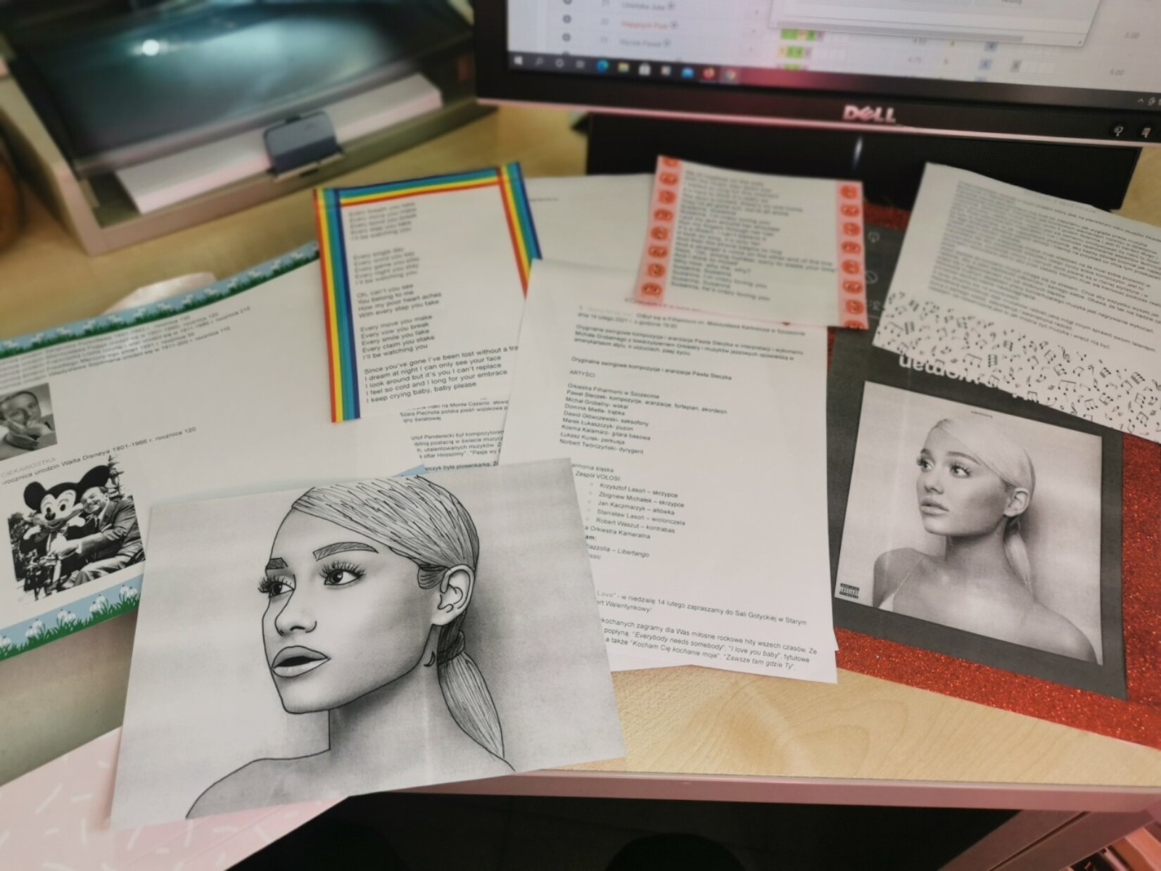 Fotografia przedstawia fragment portfolio uczennicy liceum, które zawiera drukowane teksty oraz szkice młodej kobiety - piosenkarki - ciemnoskórej kobiety o długich włosach spiętych w kucyk. Kobieta ma duże brwi oraz szeroko otwarte oczy oraz duże usta. Jest przedstawiona z półprofilu. 