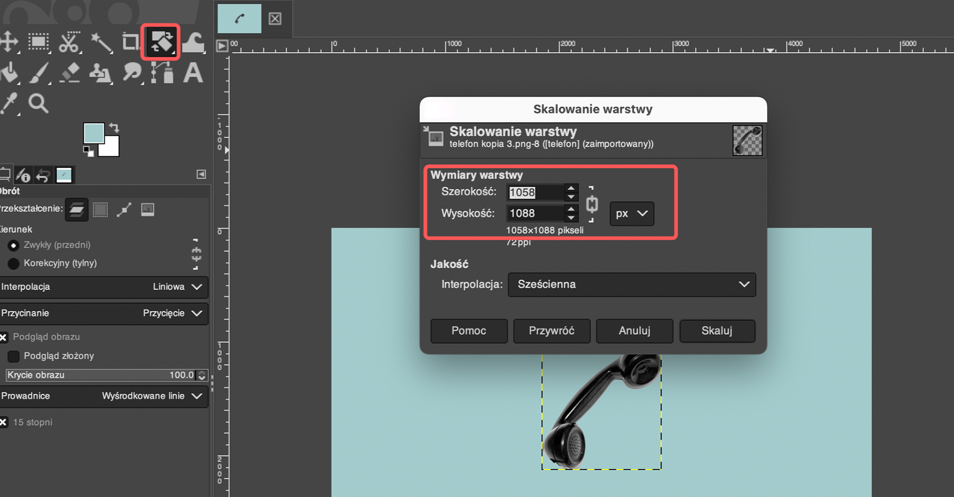 Ilustracja przedstawia okno programu. Wyróżniono ikonę obrotu. Na tle obszaru roboczego wyświetlone jest okno o nazwie: Skalowanie warstwy. Tam wyróżniono Wymiary warstwy: szerokość 1058, Wysokość 1088 pikseli. W obszarze roboczym jest niebieskie tło wraz z czarną słuchawką. Słuchawka znajduje się w kwadratowej ramce.   