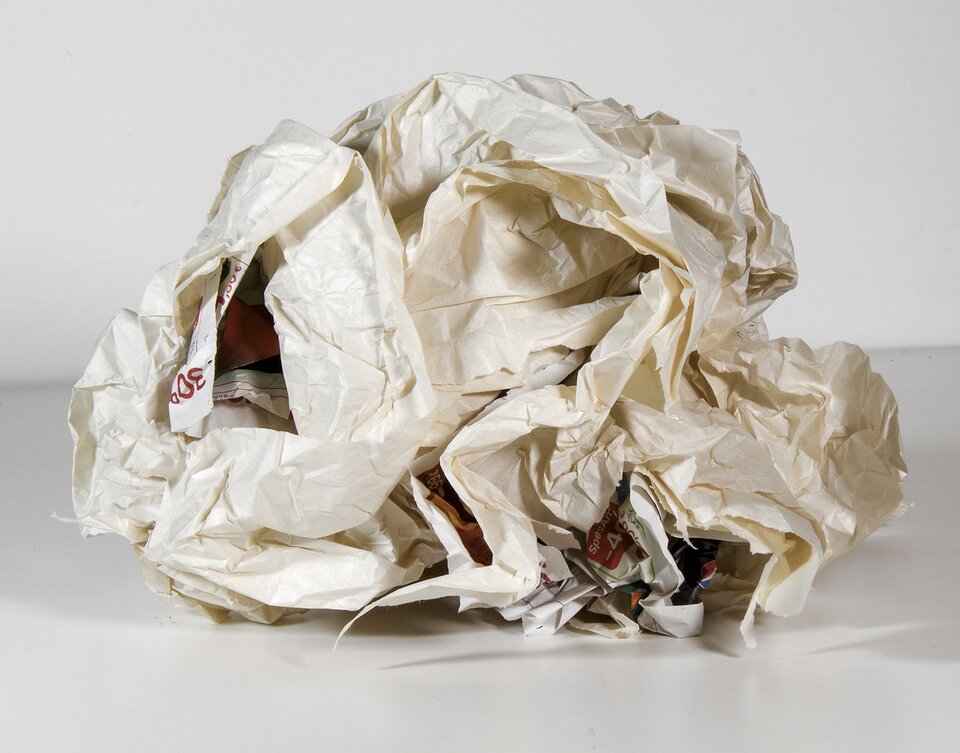 Na zdjęciu ukazano kilka kartek papieru zgniecionych w kulę, leżącą na białym stole. Na zewnątrz papier jest kremowy i gładki, natomiast z wnętrza kuli wystają kartki pokryte kolorowymi napisami.
