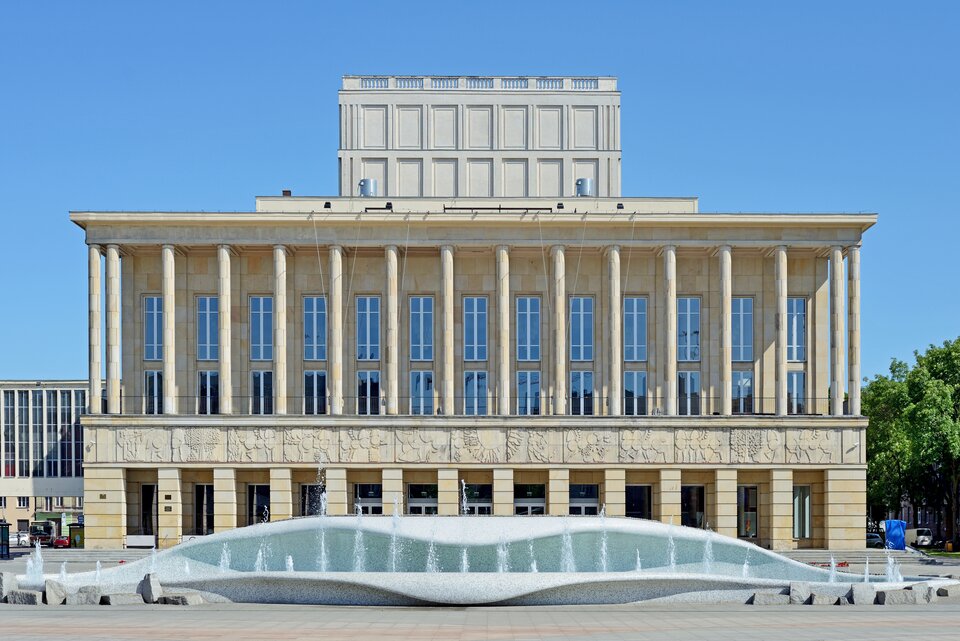 Fotografia przedstawia Teatr Wielki w Łodzi. Jest to budynek w kształcie prostokąta. Fronton o długości 50 metrów składa się z podwójnego ażuru i loggii. Główne wejście znajduje się w podcieni. Loggia opiera się o przestrzeń foyer. Górna część budynku, z wielkimi oknami, ozdobiona jest okrągłymi, wąskimi kolumnami. Dolna część krótszymi, kwadratowymi kolumnami. Pomiędzy górną, a dolną częścią znajduje się pas rzeźbiarskiego fryzu (ok. 5 m nad terenem), na którym przedstawione zostały antyczne wzory (pegazy, konie, ludzkie postacie, elementy dekoracyjne). Przed budynkiem znajduje się asymetryczna fontanna w kształcie dwóch morskich fal. Teatr Wielki jest drugim pod względem wielkości gmachem operowym w Polsce. Obecnie, widownia liczy 1074 miejsc.