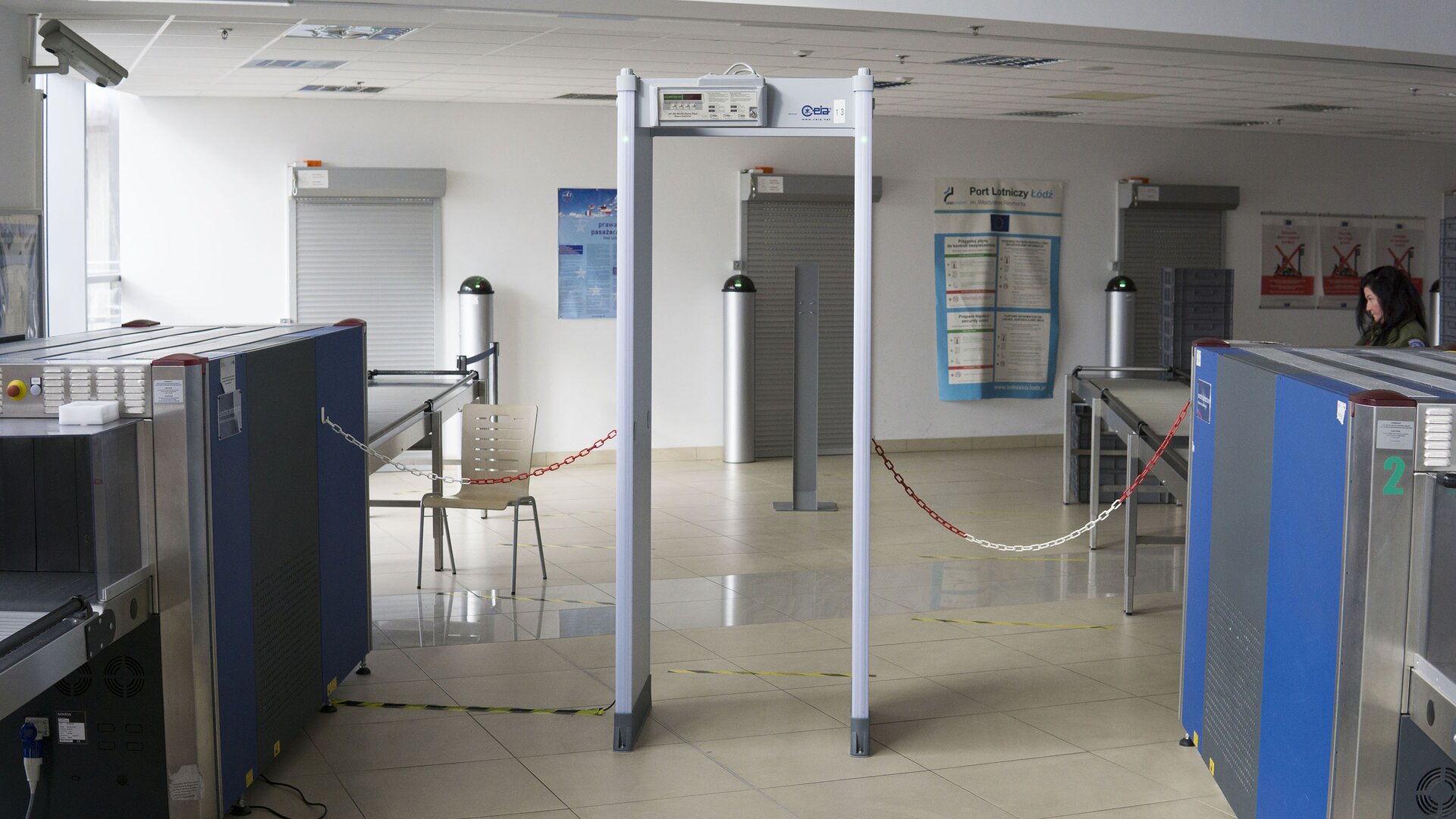 Zdjęcie przedstawia bramkę magnetyczną do kontroli osób. Ma ona kształt framugi drzwi. Kontrolowana osoba przechodzi przez nią. W przypadku wykrycia metalu, zapalają się lampki znajdujące się w górnej części brami i załącza się ostrzegawczy sygnał dźwiękowy.