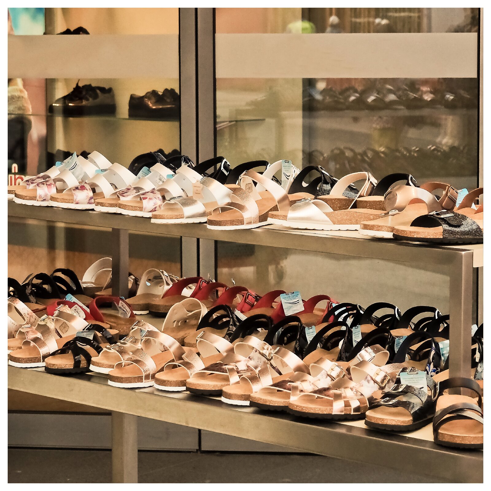 Zdjęcie przedstawia stoły z sandałami ustawionymi w sklepie obuwniczym.