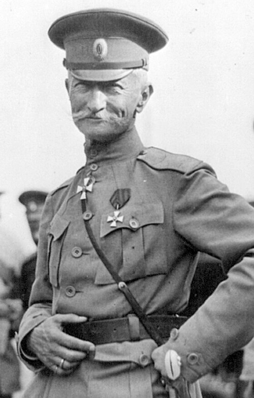 Fotografia przedstawia starszego mężczyznę w mundurze wojskowym. Ma siwe długie wąsy i czapkę z daszkiem. Jedną rękę trzyma za pasem drugą podpiera się pod bok i uśmiecha się do obiektywu. Na piersi i pod szyją wiszą dwa medale w kształcie krzyża.