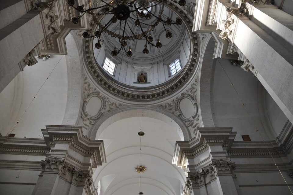 Ilustracja przedstawia wnętrze Kościoła pw św. Piotra i Pawła: kopułę sfotografowaną od dołu. Na fotografii oprócz kopuły widoczny jest fragment wnętrza budowli z górnymi partiami filarów oddzielających nawę od kaplic bocznych wraz z wydatnymi gzymsami. W bębnie kopuły widoczne są okna oraz - naprzemiennie z nimi – nisze z rzeźbami. 