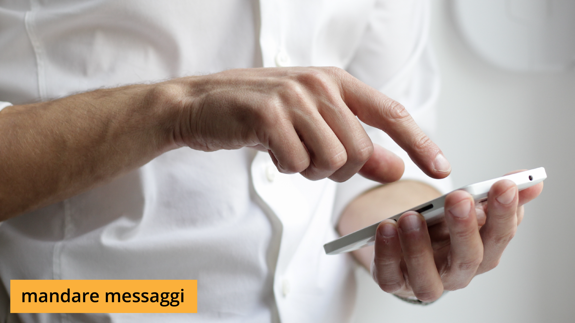 Zdjęcie przedstawia zbliżenie na ręce mężczyzny. W jednym ręku trzyma telefon komórkowy, a drugą zamierza dotknąć palcem wskazującym ekranu. Na ilustracji znajduje się napis: mandare messaggi.