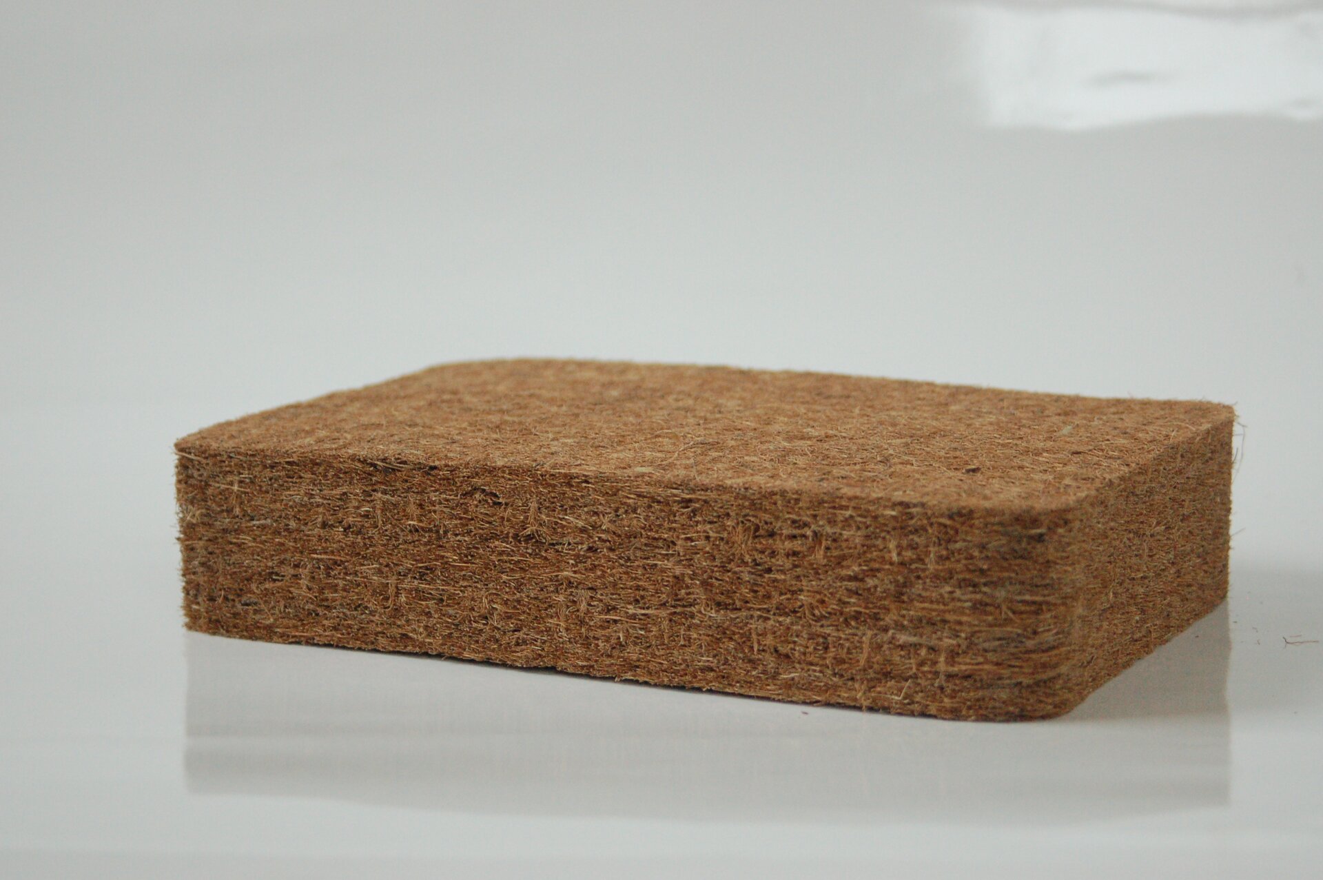 Zdjęcie przedstawia włókno kokosowe zbite w brązowy płaski prostopadłościan o dużej grubości, widziany z boku.