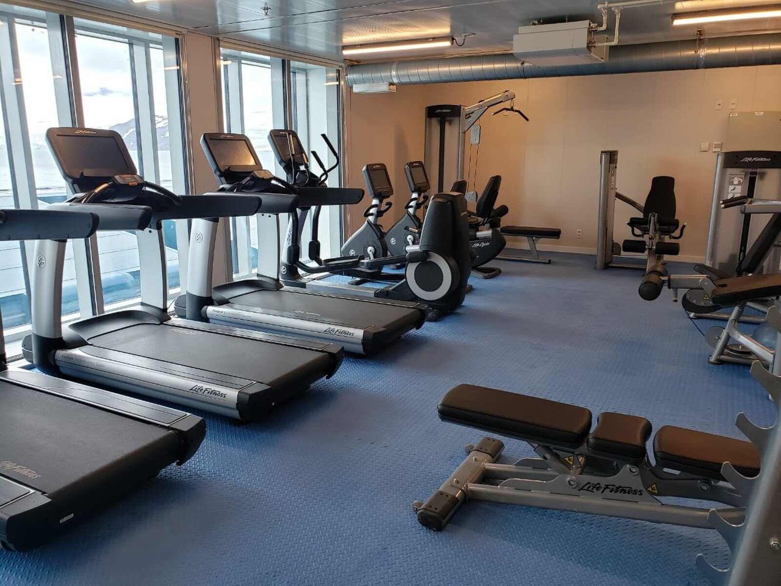 Fotografia przedstawiająca pomieszczenie ze sprzętem do treningu, między innymi z bieżniami i rowerami stacjonarnymi.