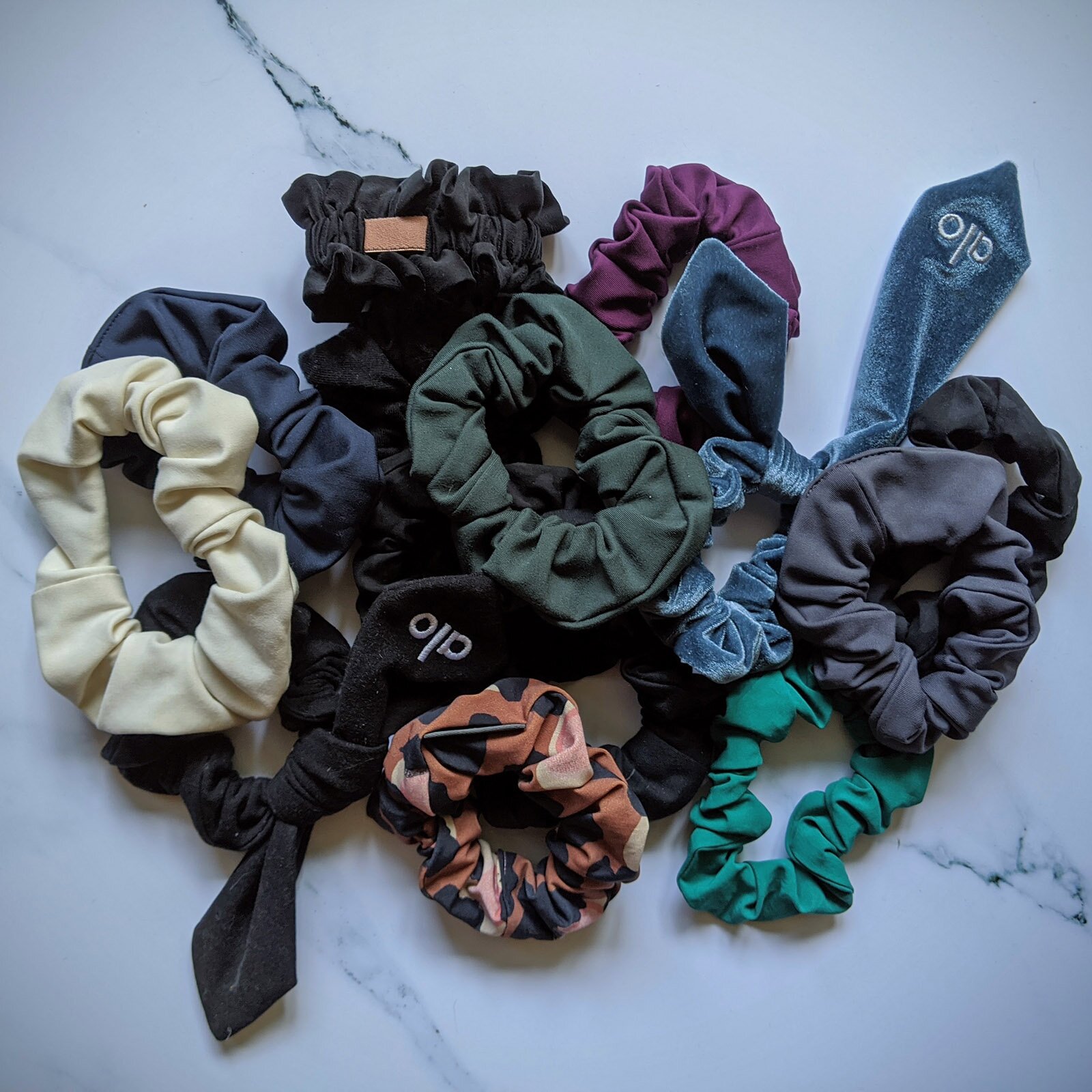 Zdjęcie przedstawia różnokolorowe gumki i frotki do włosów. Widoczne są gumki obszyte drapowanym materiałem oraz zakończone zwisającymi elementami w formie krawata. 