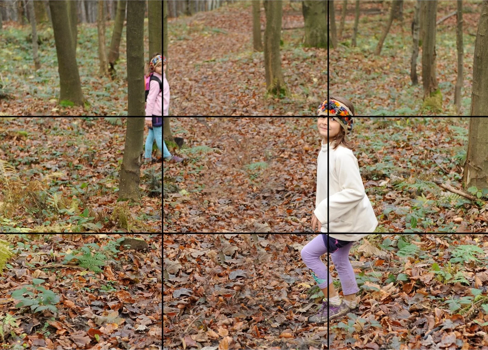 Fotografia przedstawiająca dzieci w jesiennym lesie z nałożonym na zdjęcie trójpodziałem kadru w postaci czarnych linii. Przecięcia linii wskazują mocne punkty. Jedno z przecięć linii znajduje się na twarzy dziecka znajdującego się na pierwszym planie, drugie przecina jego udo. Trzeci mocny punkt znajduje się na dziewczynce stojącej w tle, a czwarte na liściastej ziemi. 