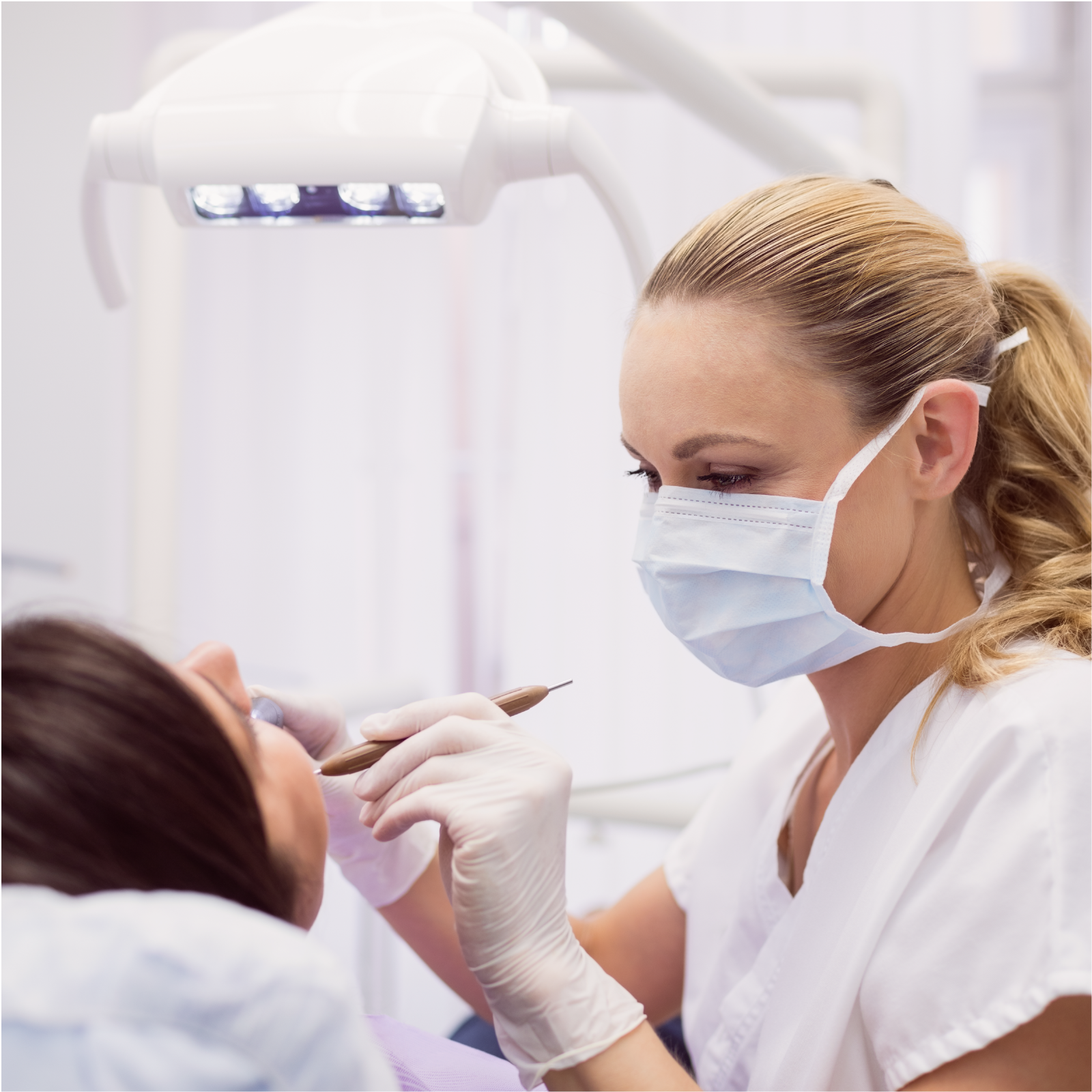 Zdjęcie przedstawia panią dentystkę w maseczce na ustach i rękawiczkach na dłoniach, która przeprowadza zabieg w ustach pacjenta siedzącego prze nią.