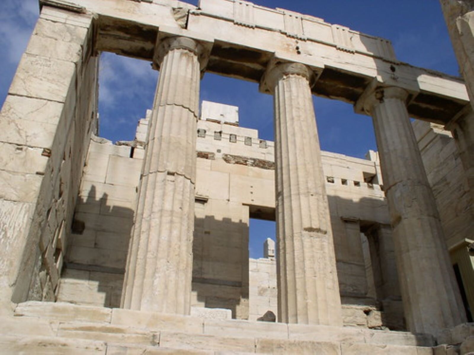 Fotografia przedstawia monumentalne, kamienne kolumny, wspierające kamienne belkowanie greckiej budowli. To fragment Propylejów, majestatycznej bramy z kolumnadą, która prowadziła na Akropol ateński.