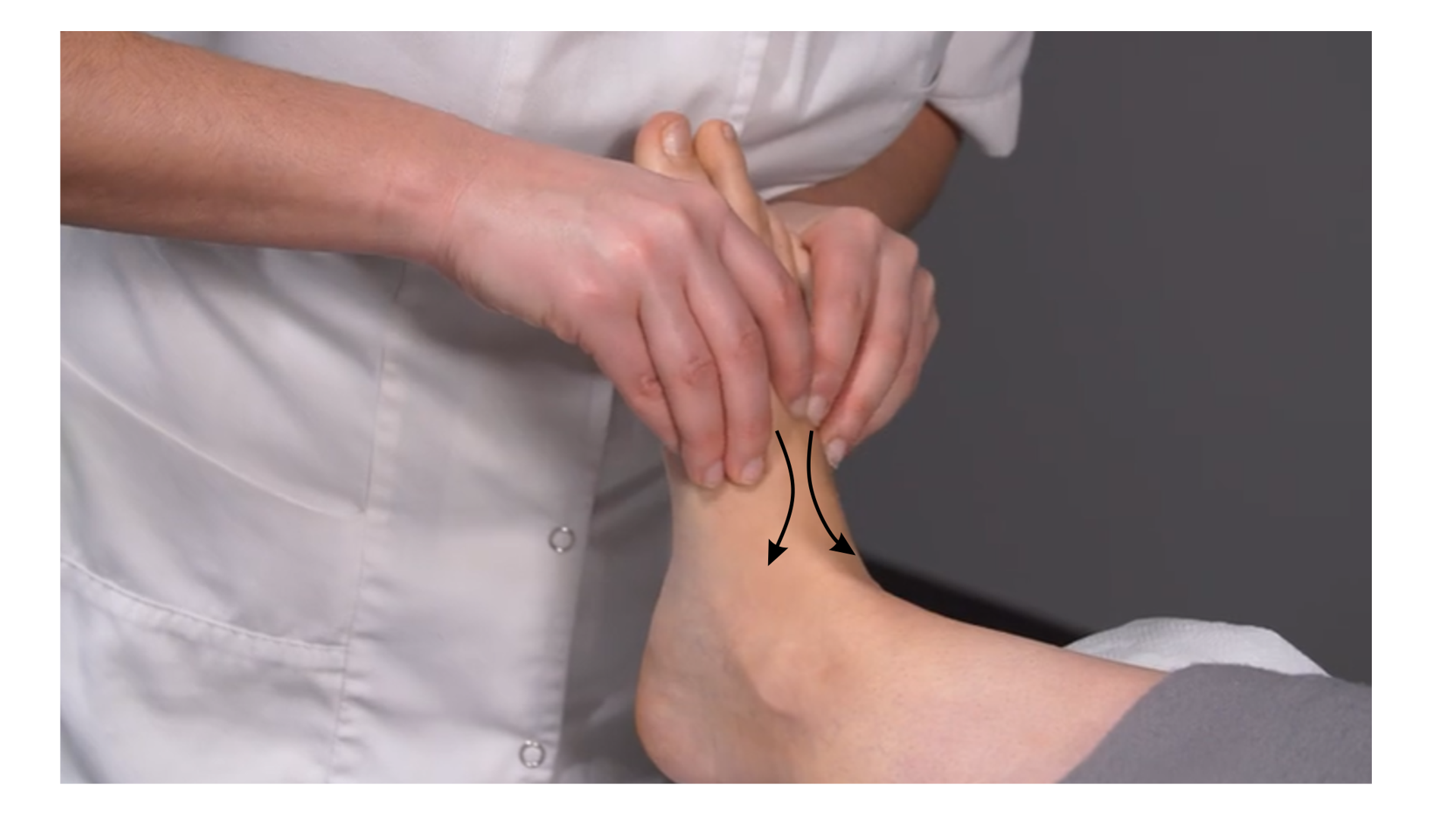 Zdjęcie przedstawia lewą stopę pacjenta leżącego tyłem na stole do masażu. Masażysta wykonuje ruch opuszkami palców obu rąk od palców stopy w stronę kostek bocznych. 