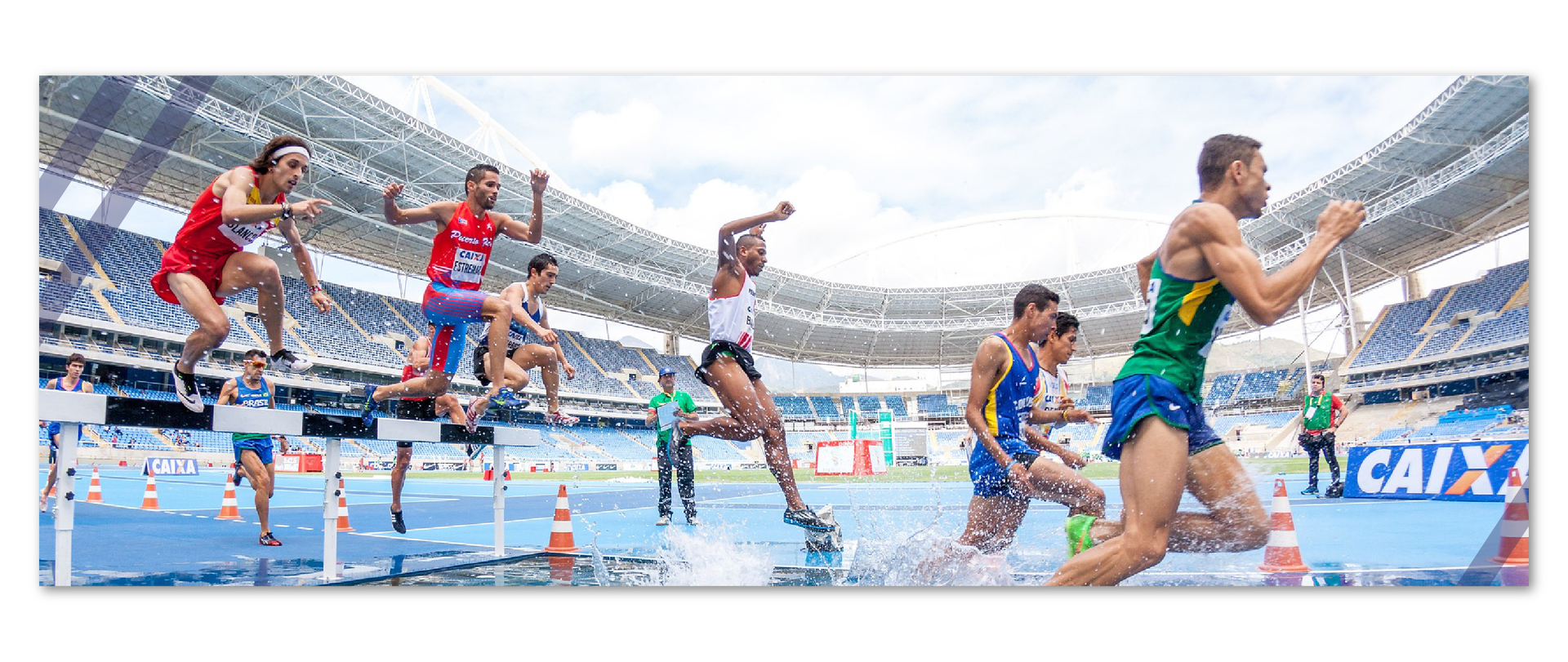 Na fotografii są lekkoatleci skaczący przez płotki, znajdujący się w różnych fazach skoku. Niektórzy z nich znajdują się przed płotkiem z biało – czarną poprzeczką, niektórzy nad nią przeskakują, a pozostali są już na ziemi. Pod ich nogami widać rozpryśniętą wodę. W tle znajduje się stadion oraz puste trybuny. 