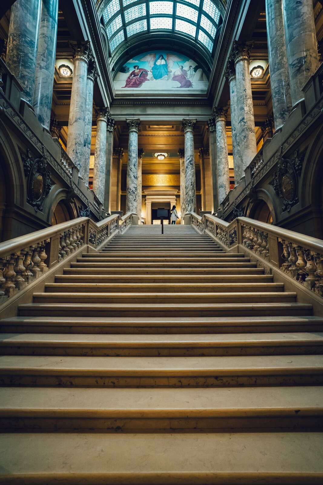 Grafika przedstawia z frontowej strony, szerokie kamienne schody, poręczami bo obu stronach. Nad schodami w półokręgu znajdują się małe prostokątne okna, natomiast po lewej i prawej stronie są umieszczone marmurowe kolumny.