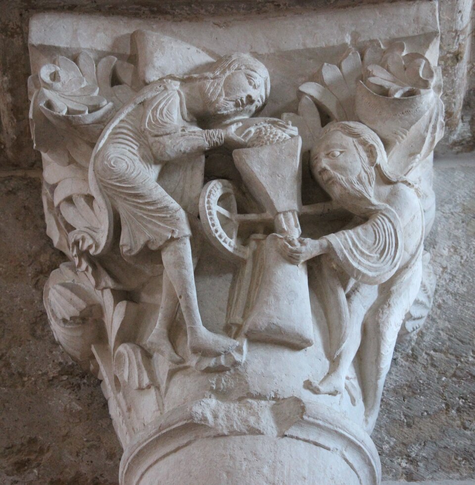 Ilustracja przedstawia kapitel ze sceną z mistycznego młyna bazyliki św. Marii Magdaleny w Vézelay. Zdjęcie ukazuje rzeźbę, na której znajdują się dwie postacie, ujęte z profilu, podczas wspólnej pracy.