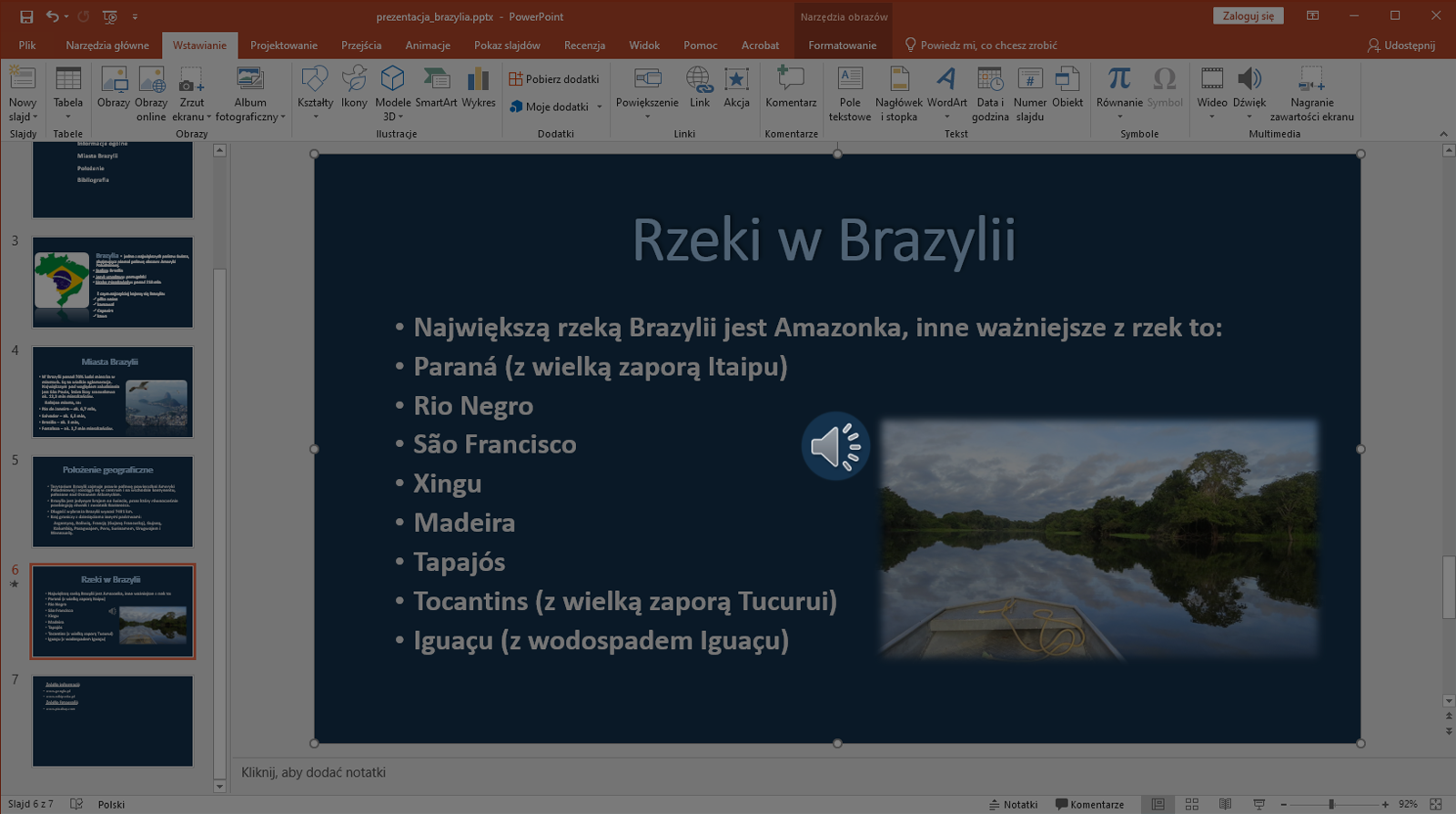 Zrzut ekranu przedstawia wycinek okna programu Microsoft PowerPoint. Prezentacja zapisana jest jako prezentacja brazylia.pttx. W programie znajdują się zakładki takie jak „Plik”, „Narzędzie główne”, „Wstawianie”, „Projektowanie”, „Przejścia”, Animacje”, „Pokaz slajdów”. Recenzje”, „Widok”, „Pomoc”, „Acrobat” , "Formatowanie" oraz „Powiedz mi, co chcesz zrobić”.  Po lewej stronie znajduje się lista slajdów. Prezentacja składa się aktualnie z siedmiu slajdów. Wybrano slajd szósty. Na większości okna programu znajduje się powiększony slajd szósty o nazwie Rzeki w Brazylii. Na slajdzie zapisano nazwy rzek w Brazylii. Pod slajdem znajduje się miejsce na notatkę. Całe okno prezentacji jest wyciemnione. Na środku slajdu pojawia się ikonka głośnika.  