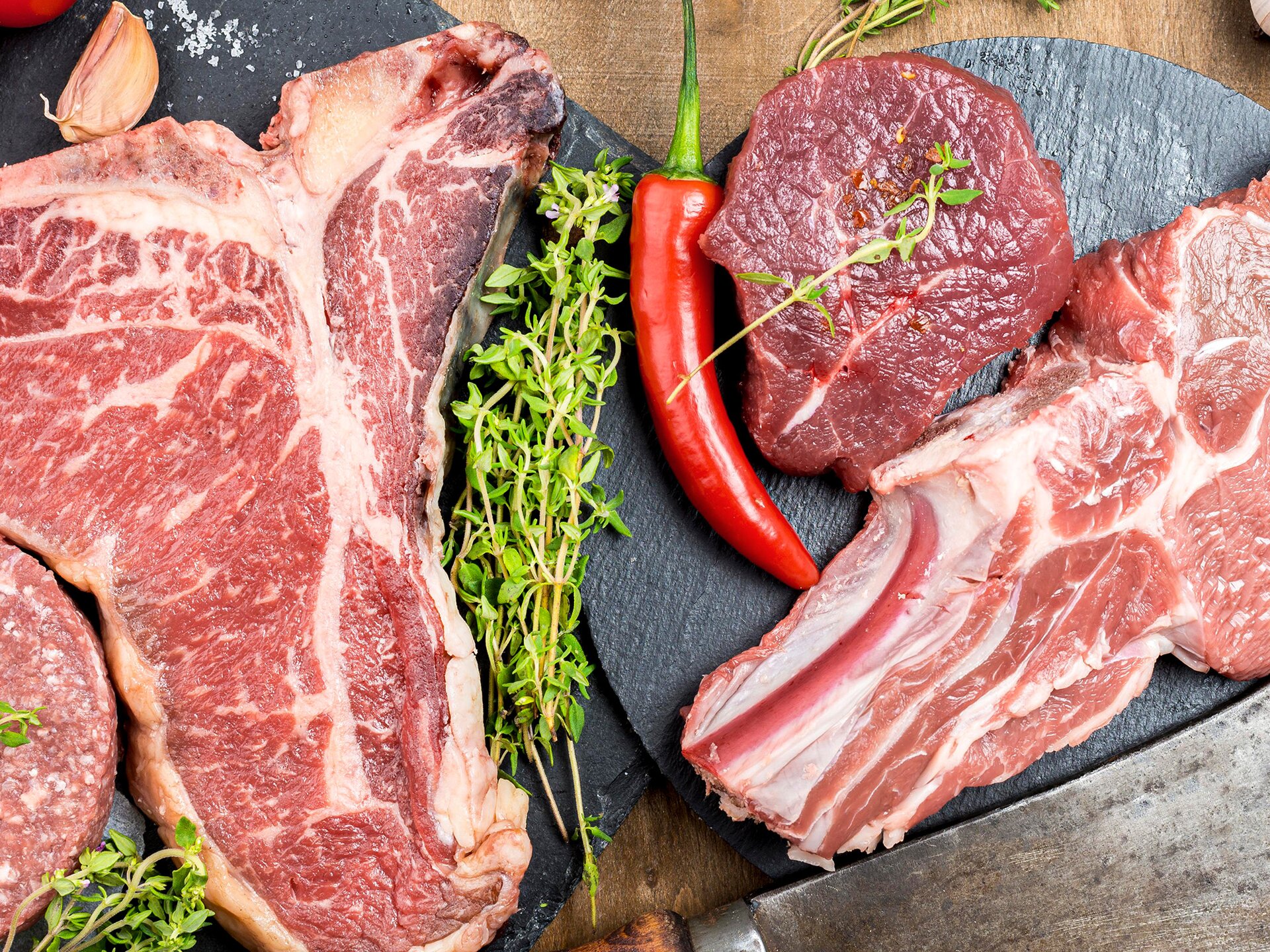 Zdjęcie przedstawia różne gatunki mięsa, pokrojone na plastry. Widoczna jest również czerwona papryczka i gałązki tymianku.