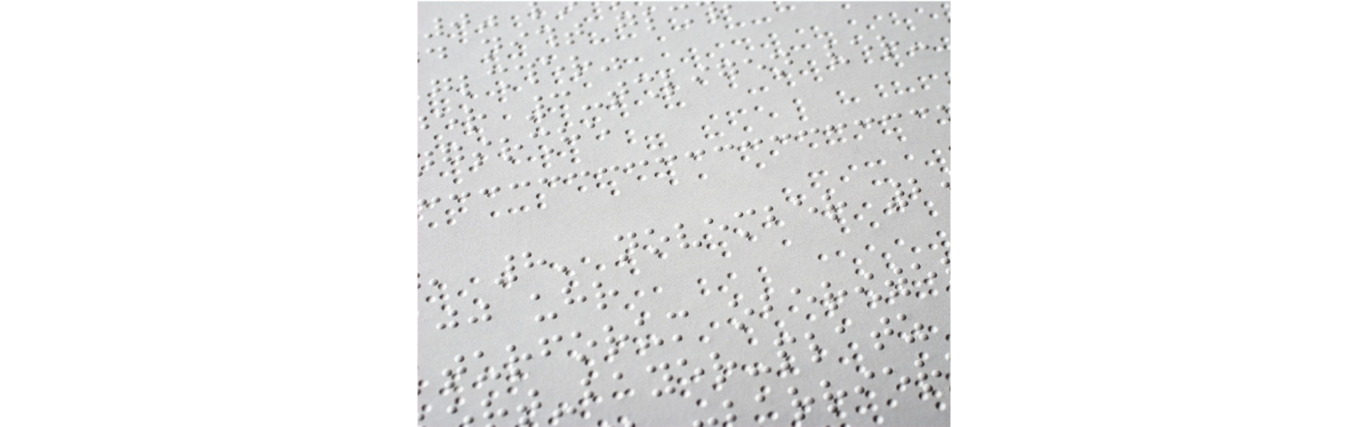 Zdjęcie przedstawia fragment białego arkusza z treścią zapisaną pismem Braille'a. Na arkuszu widoczne są wypukłe i wklęsłe punkty, które odpowiadają literom alfabetu oraz znakom interpunkcyjnym i pomocniczym.  