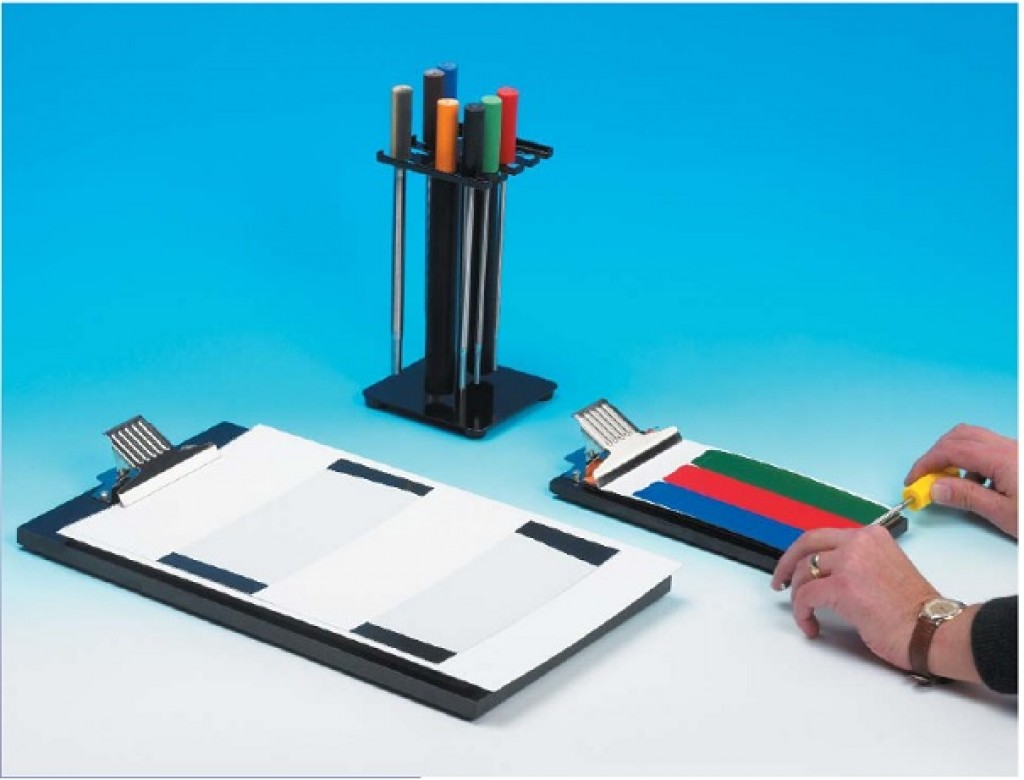 Na zdjęciu ukazana jest powlekarka ręczna (prętowa). Widoczny jest statyw, na którym znajdują się podłużne pręty z kolorowymi końcówkami. Obok widać podkładki z kartkami z różnymi kolorami.