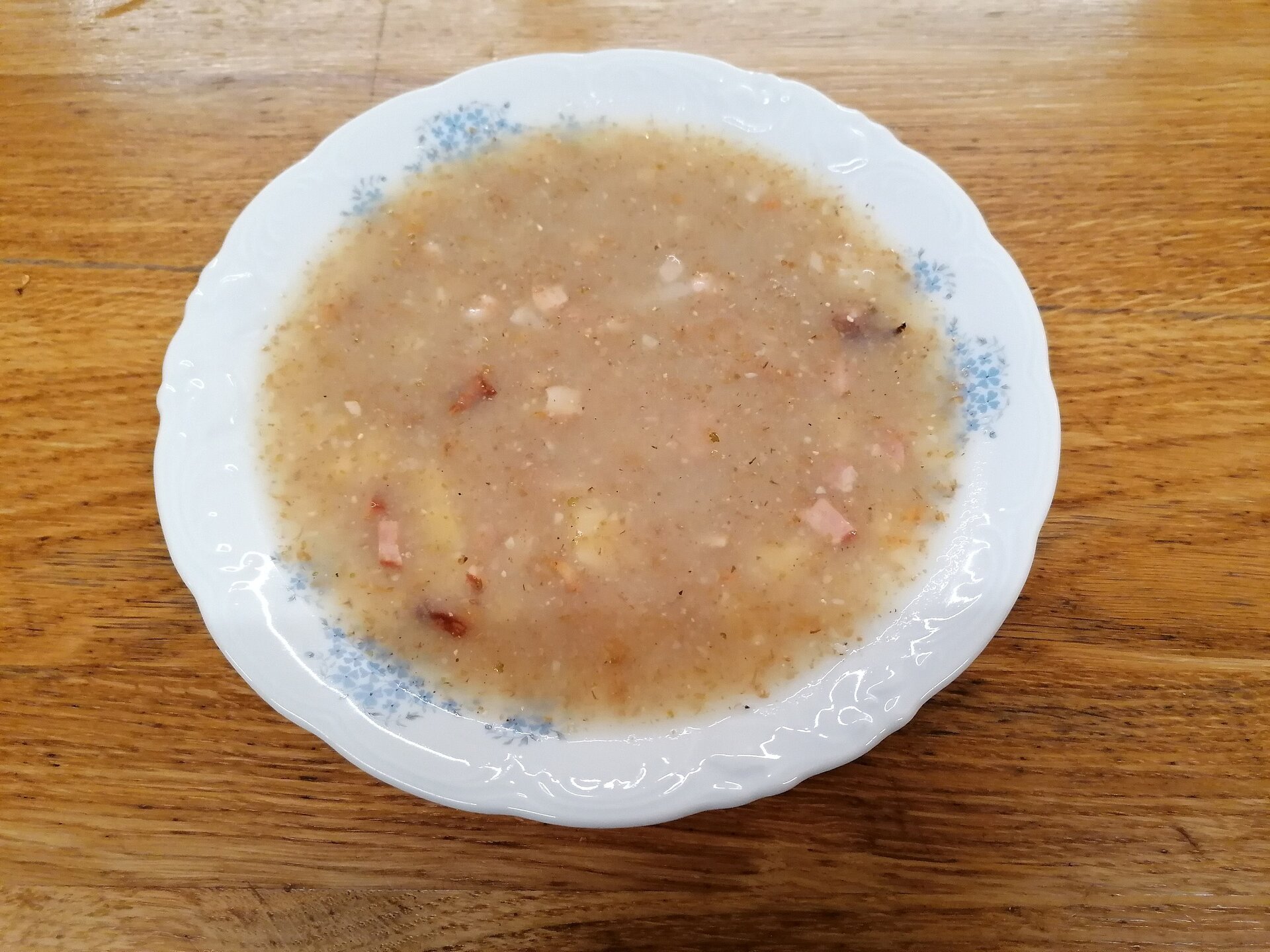 Zdjęcie talerza z żurkiem. W zupie pływają kawałki kiełbasy i ziemniaki.