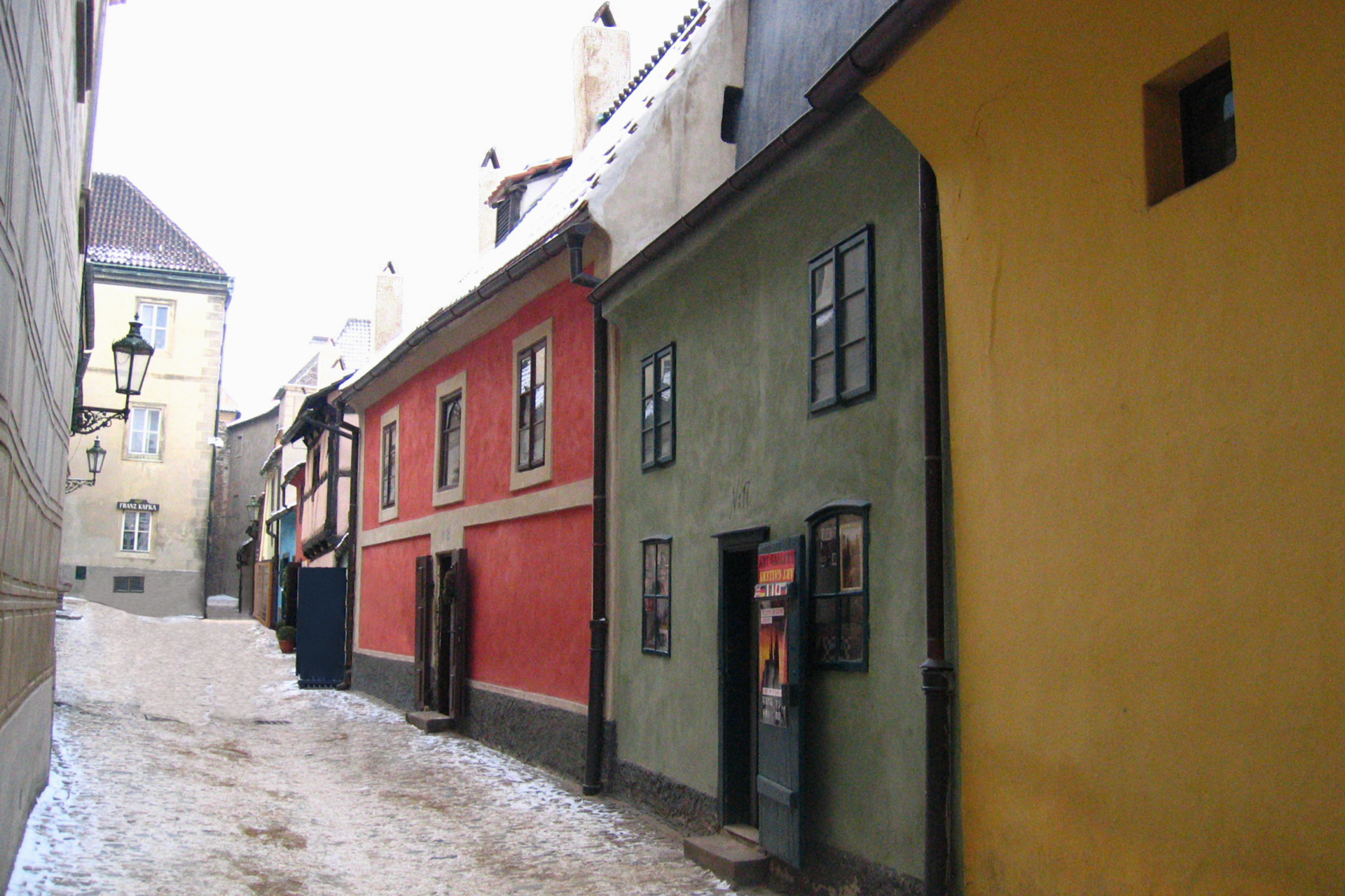 Zdjęcie praskiej Złotej Uliczki zimą. Przedstawia ten sam ciąg budynków, co poprzednie, lecz od drugiej strony i z uliczką przysypaną śniegiem. Fotograf stał pod budynkiem w kolorze jaskrawej żółci, a kolejne domy są w kolorze morskim, czerwonym, brązowym, niebieskim i kanarkowym. Wymieniony w opisie poprzedniego zdjęcia dom turkusowy jest cofnięty względem pozostałych i z tej perspektywy niewidoczny.