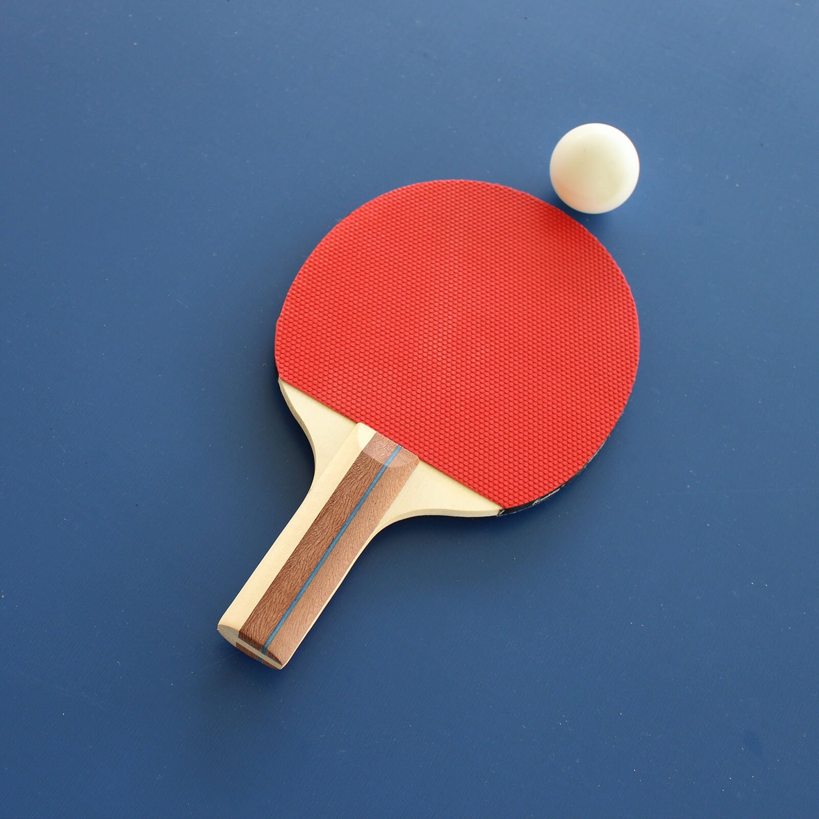 Ilustracja przedstawia czerwoną paletkę do ping‑ponga, obok której leży biała piłeczka ping‑pongowa.