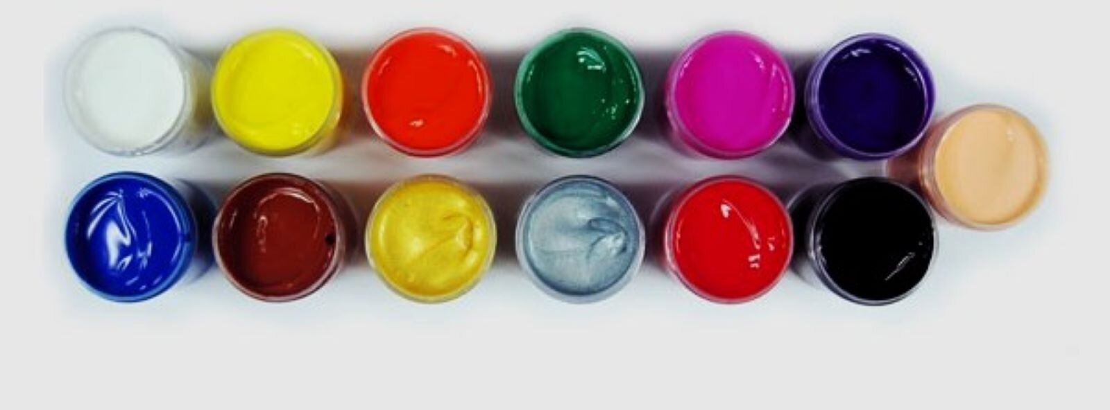 Zdjęcie z góry pokazuje 13 słoiczków z farbami plakatowymi. Ustawione są równo obok siebie w dwóch rzędach, mają otwarte przykrywki, są pełne gęstej farby. To komplet farb bez pudełka. 