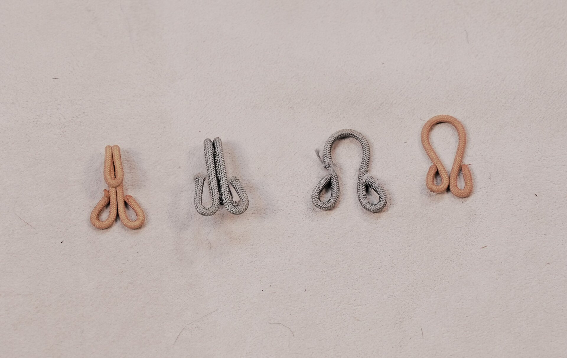 Zdjęcie przedstawia cztery haftki w odcieniach szarości i brązu. Dwie z haftek posiadają haczyki. 