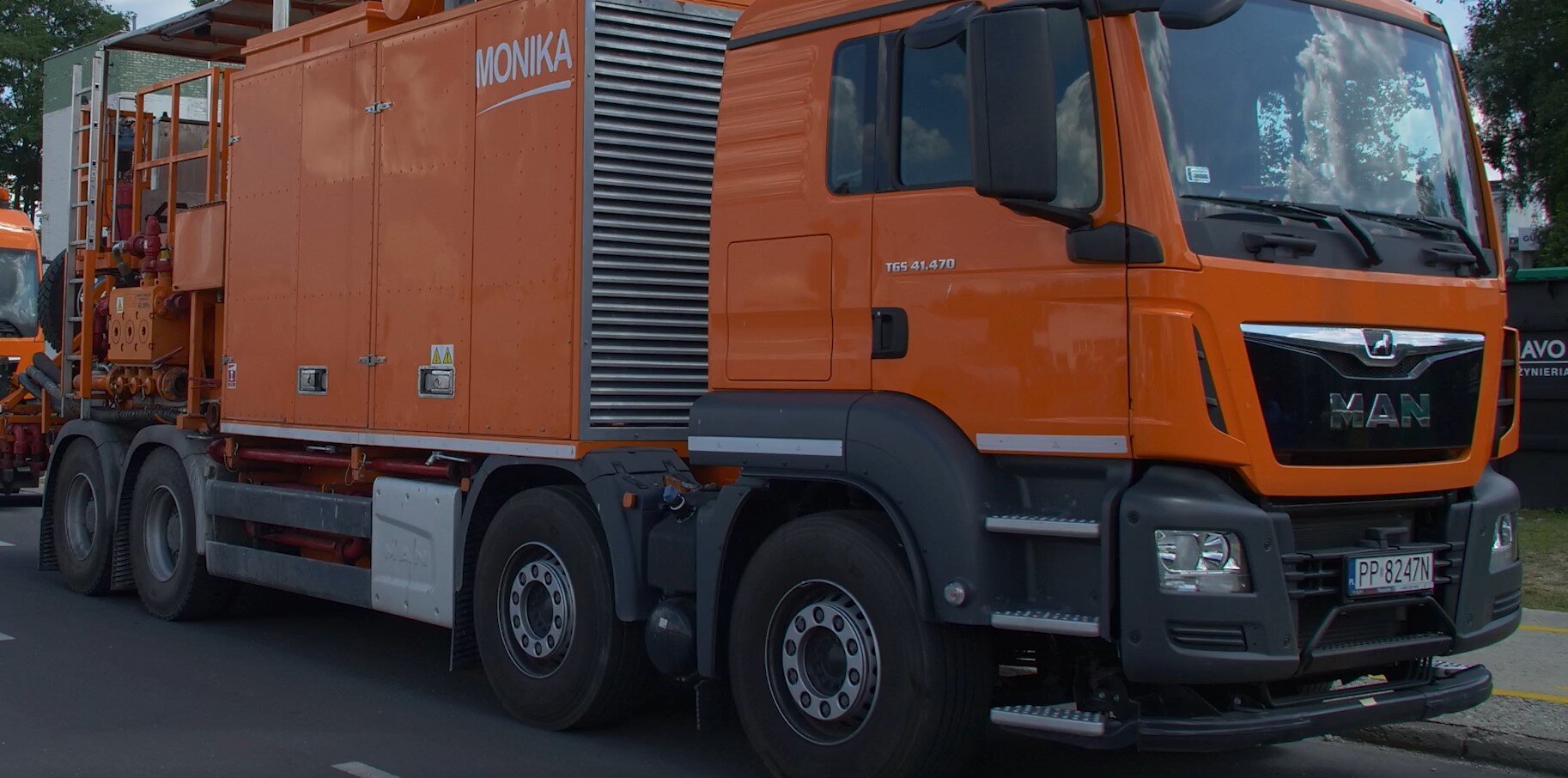 Na zdjęciu widać agregat cementacyjny na podwoziu samochodowym widzianym pod kątem od strony kabiny kierowcy.Agregat osadzony jest na podwoziu samochodowym, które ma cztery koła po każdej ze stron. Za kabiną kierowcy znajduje się duży pomarańczowy element o kształcie prostopadłościanu. Z przodu elementu są drzwi. Z tyłu podwozia samochodowego widać drabinę, rury oraz gumowe węże. Drabina jest przytwierdzona do boku samochodu.