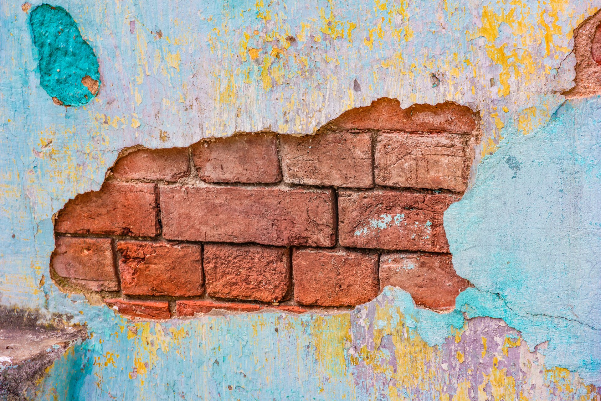 Zdjęcie przedstawia uszkodzenia tynków. Widoczne jest spore pęknięcie w tynku na ścianie. Pod spodem widać cegły. Widać też pęknięcia w tynku.