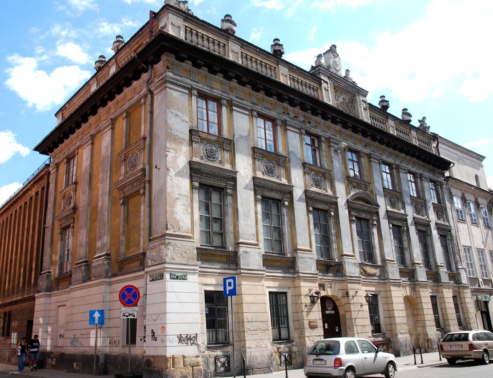 Na zdjęciu wczesnoklasycystyczny pałac. Fasada budynku jest bogato dekorowana. Nad oknami na piętrze znajdują się okrągłe, kamienne płaskorzeźby z motywem roślinnym. Dach wykończony jest kamiennymi figurami.