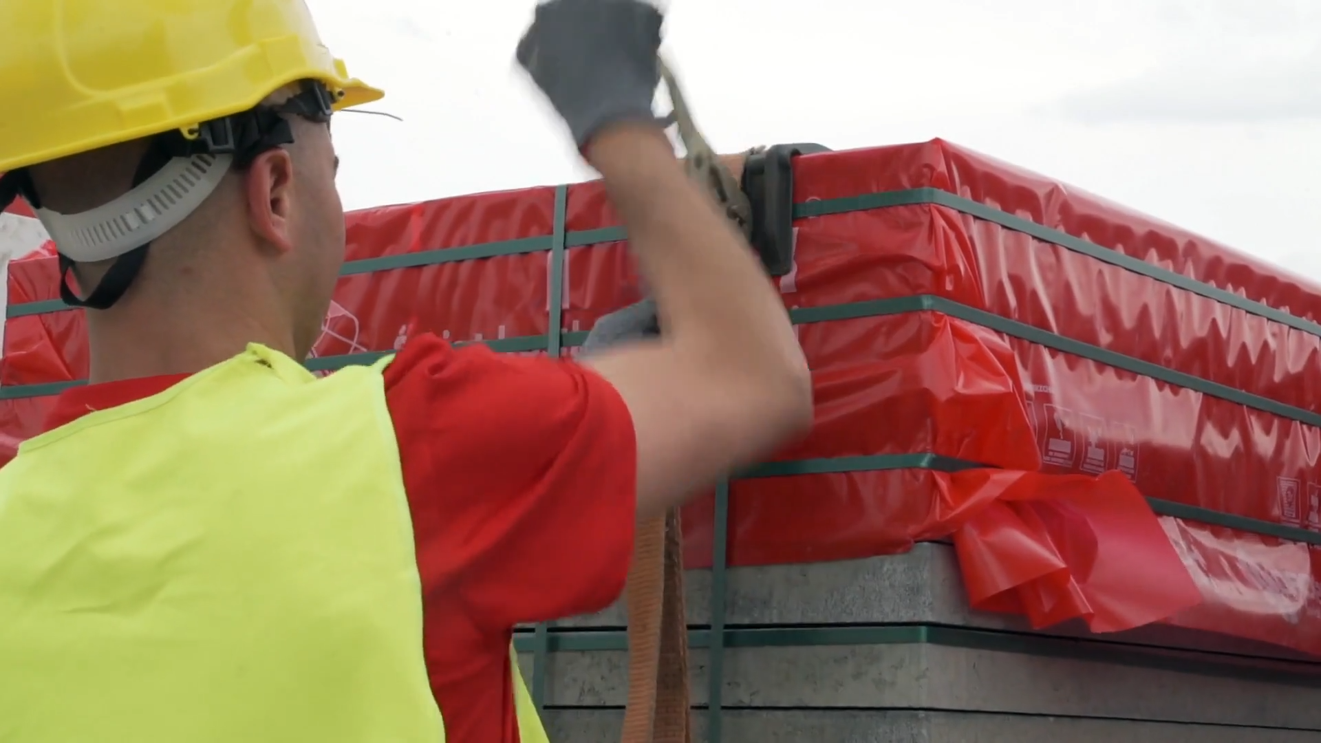 Zdjęcie przedstawia pracownika w żółtym kasku oraz kamizelce odblaskowej, który zabezpiecza towar do transportu.